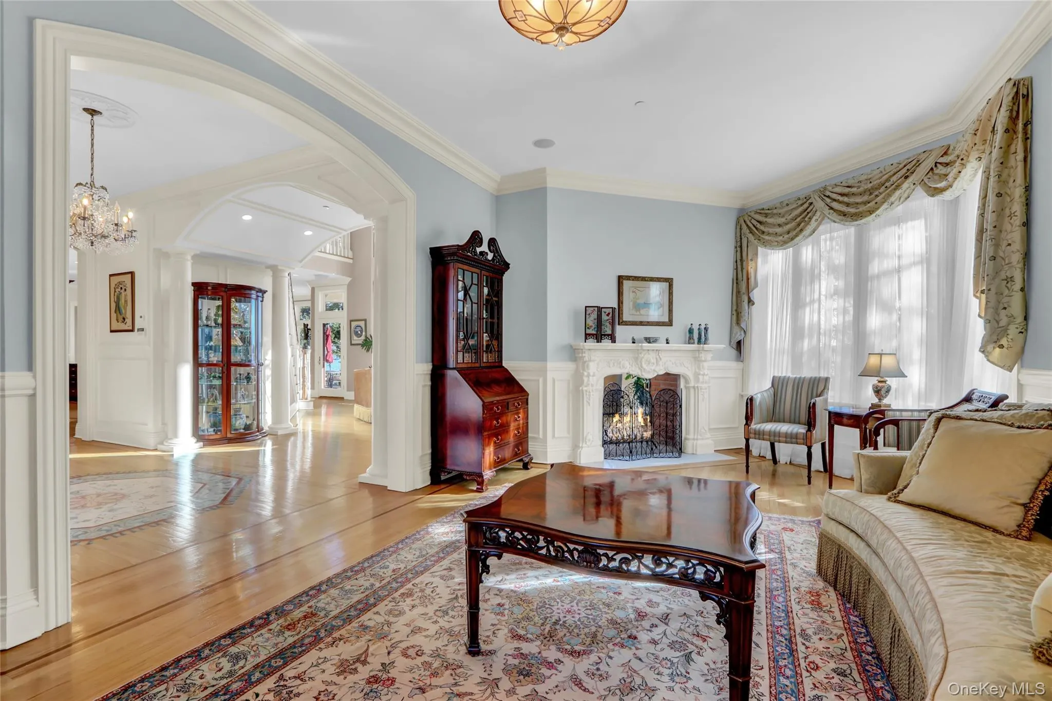 Living room featuring decorative columns, wood finished floors, a lit fireplace, and crown molding Living room featuring decorative columns, wood finished floors, a lit fireplace, and crown molding