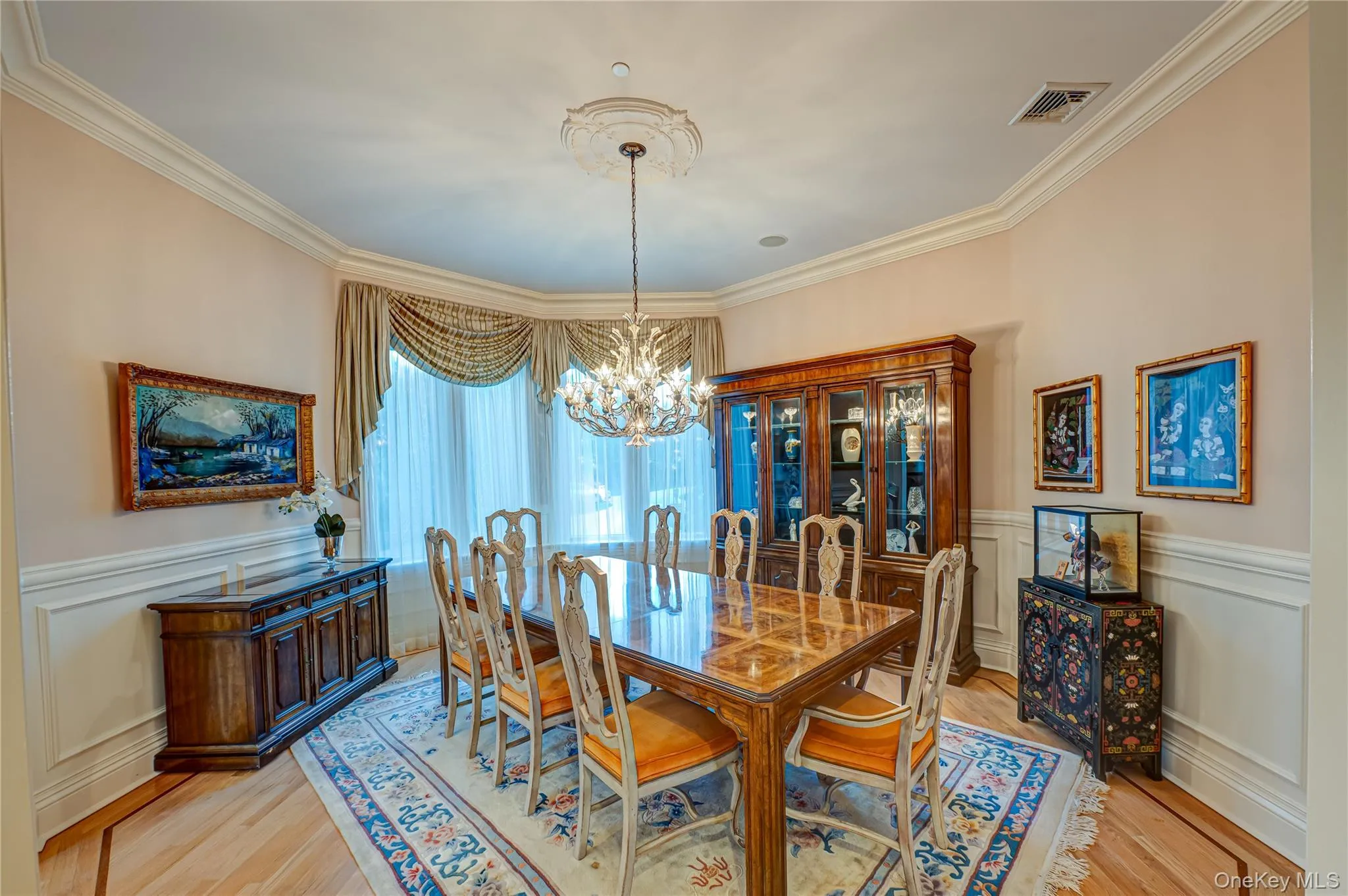 Dining room with visible vents, crown molding, light wood-type flooring, a wainscoted wall, and an inviting chandelier Dining room with visible vents, crown molding, light wood-type flooring, a wainscoted wall, and an inviting chandelier