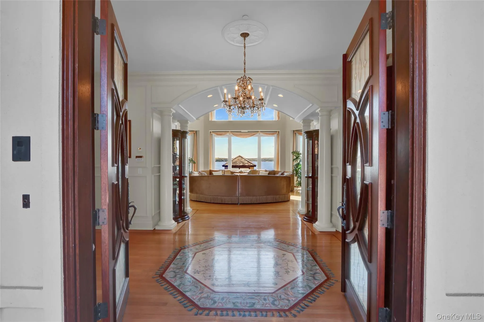 Entryway featuring a notable chandelier, crown molding, light wood-style flooring, ornate columns, and arched walkways Entryway featuring a notable chandelier, crown molding, light wood-style flooring, ornate columns, and arched walkways