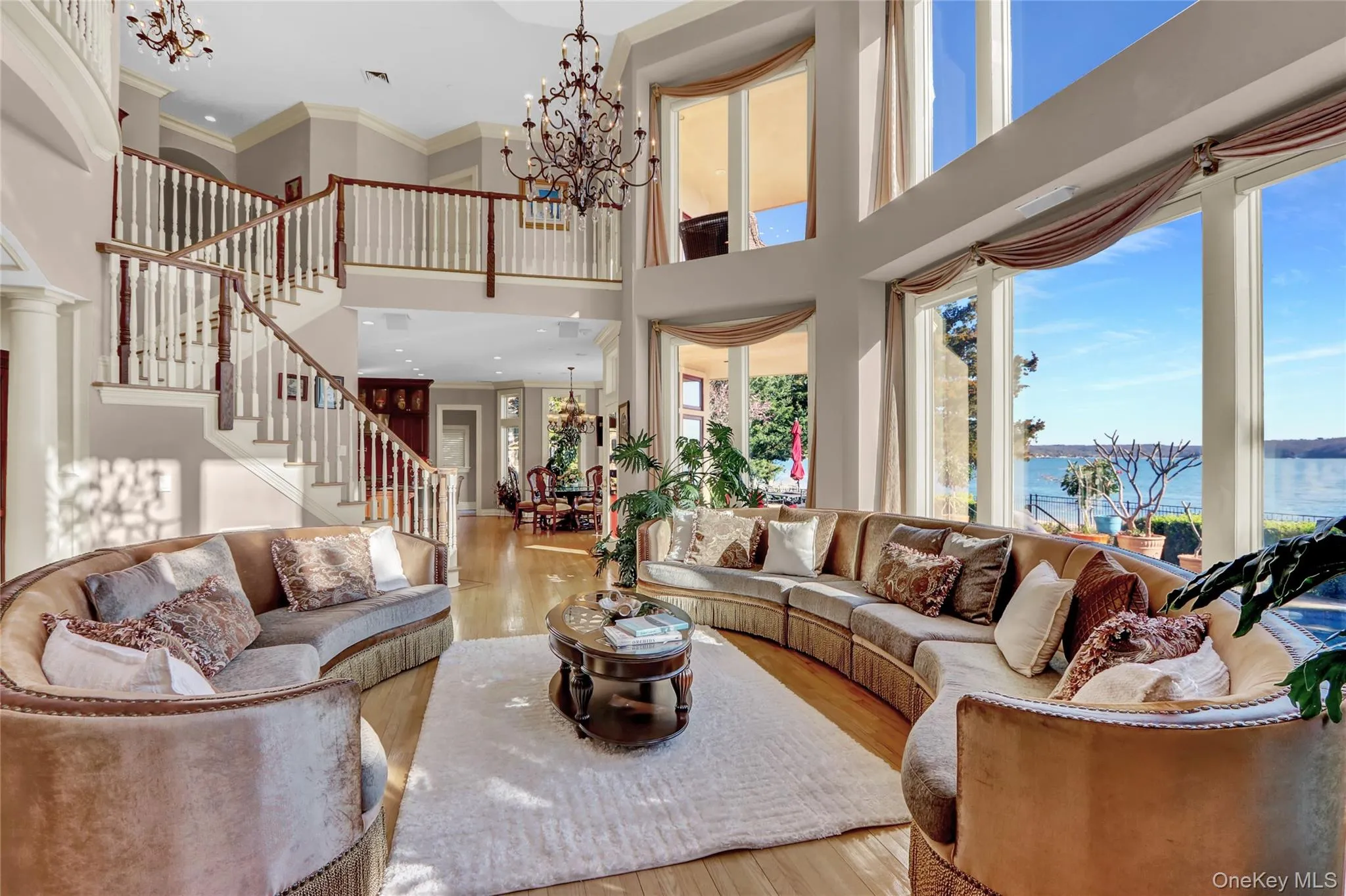 Living room featuring an inviting chandelier, stairway, wood-type flooring, ornamental molding, and a towering ceiling Living room featuring an inviting chandelier, stairway, wood-type flooring, ornamental molding, and a towering ceiling
