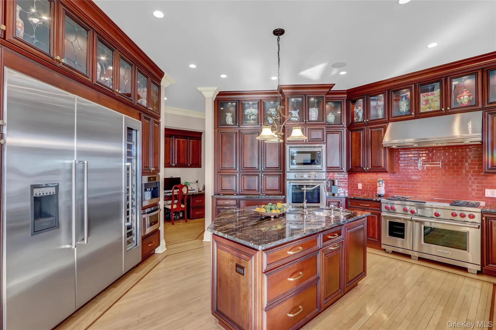 Kitchen with reddish brown cabinets, decorative light fixtures, under cabinet range hood, built in appliances, and light wood-type flooring Kitchen with reddish brown cabinets, decorative light fixtures, under cabinet range hood, built in appliances, and light wood-type flooring