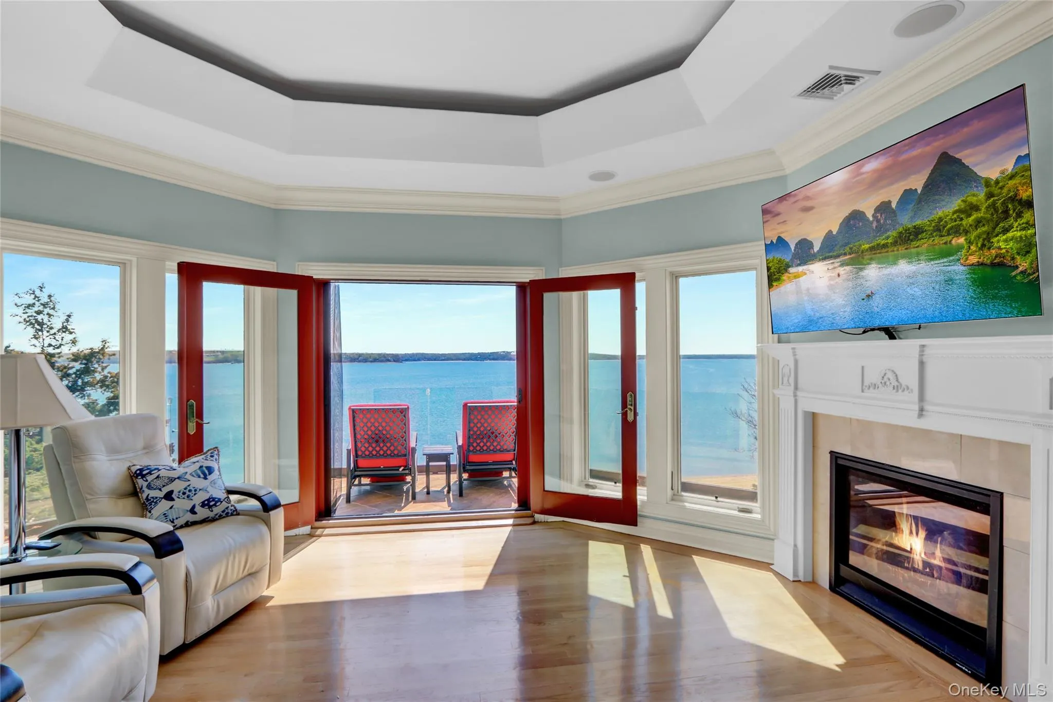 Living area featuring a glass covered fireplace, a raised ceiling, a wealth of natural light, and visible vents Living area featuring a glass covered fireplace, a raised ceiling, a wealth of natural light, and visible vents