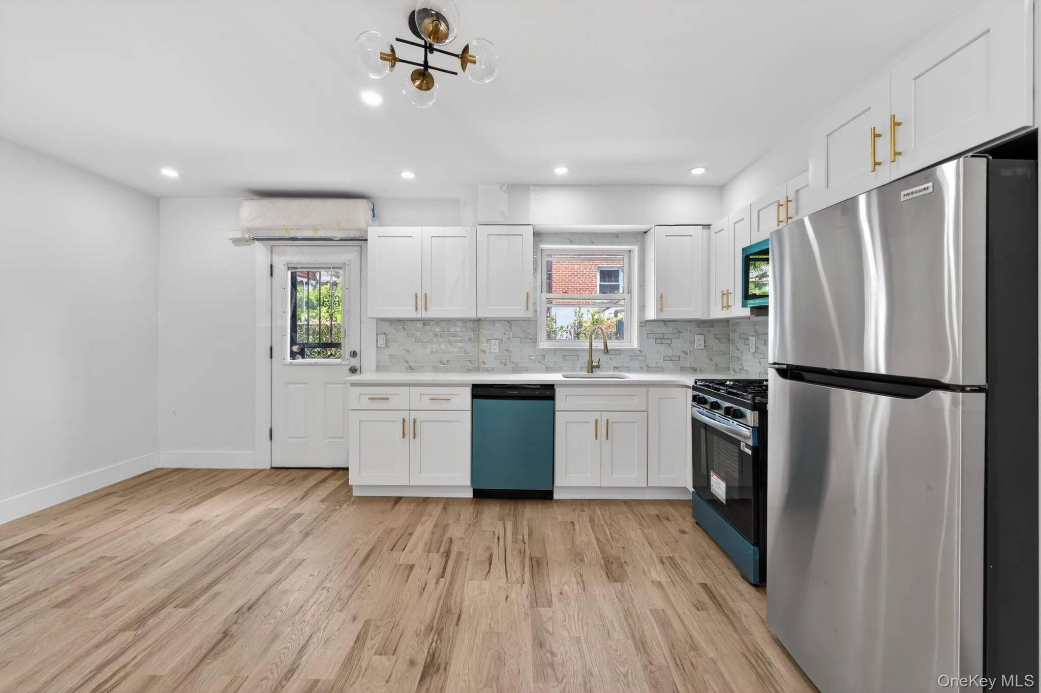 Modern kitchen featuring white shaker cabinetry, stainless steel appliances, a unique teal dishwasher and range, and light wood-finish flooring Modern kitchen featuring white shaker cabinetry, stainless steel appliances, a unique teal dishwasher and range, and light wood-finish flooring