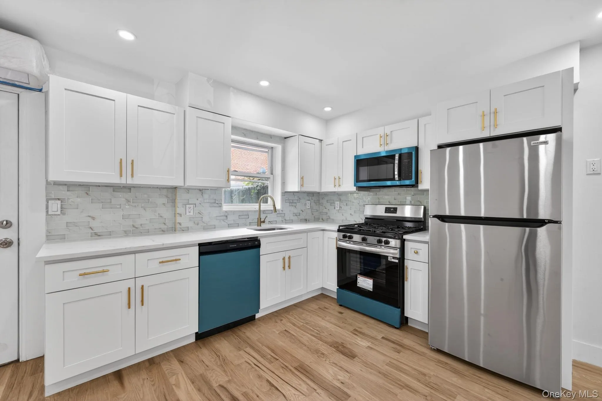 Kitchen featuring white shaker cabinetry, quartz countertops, a mosaic tile backsplash, stainless steel appliances, and wood-finish flooring Kitchen featuring white shaker cabinetry, quartz countertops, a mosaic tile backsplash, stainless steel appliances, and wood-finish flooring