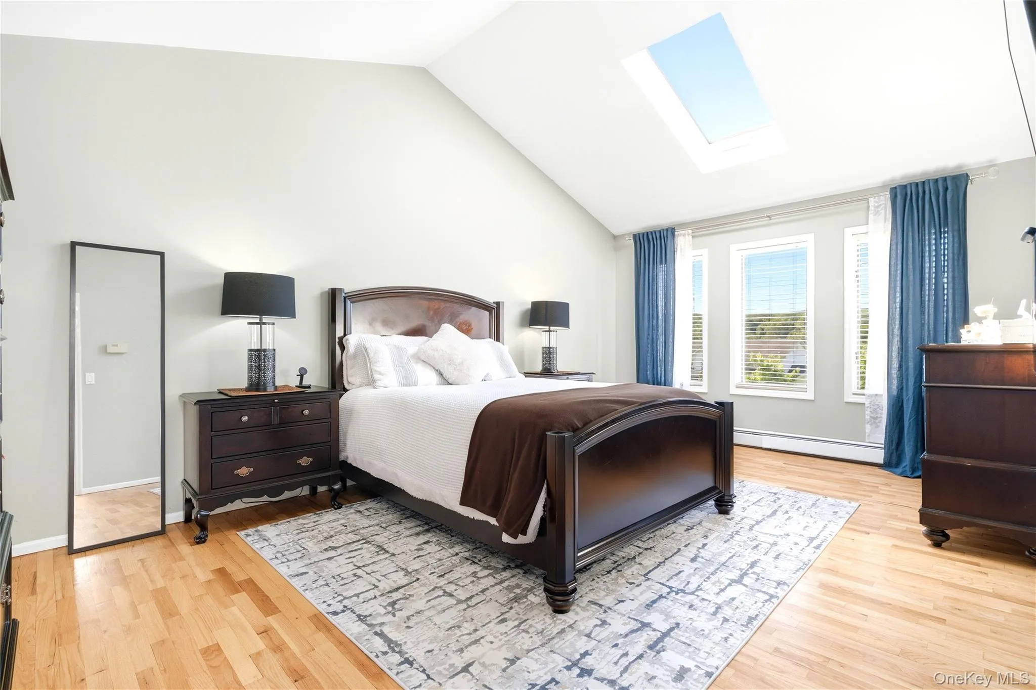 Bedroom featuring a skylight, vaulted ceiling, baseboard heating, and light wood-style flooring Bedroom featuring a skylight, vaulted ceiling, baseboard heating, and light wood-style flooring