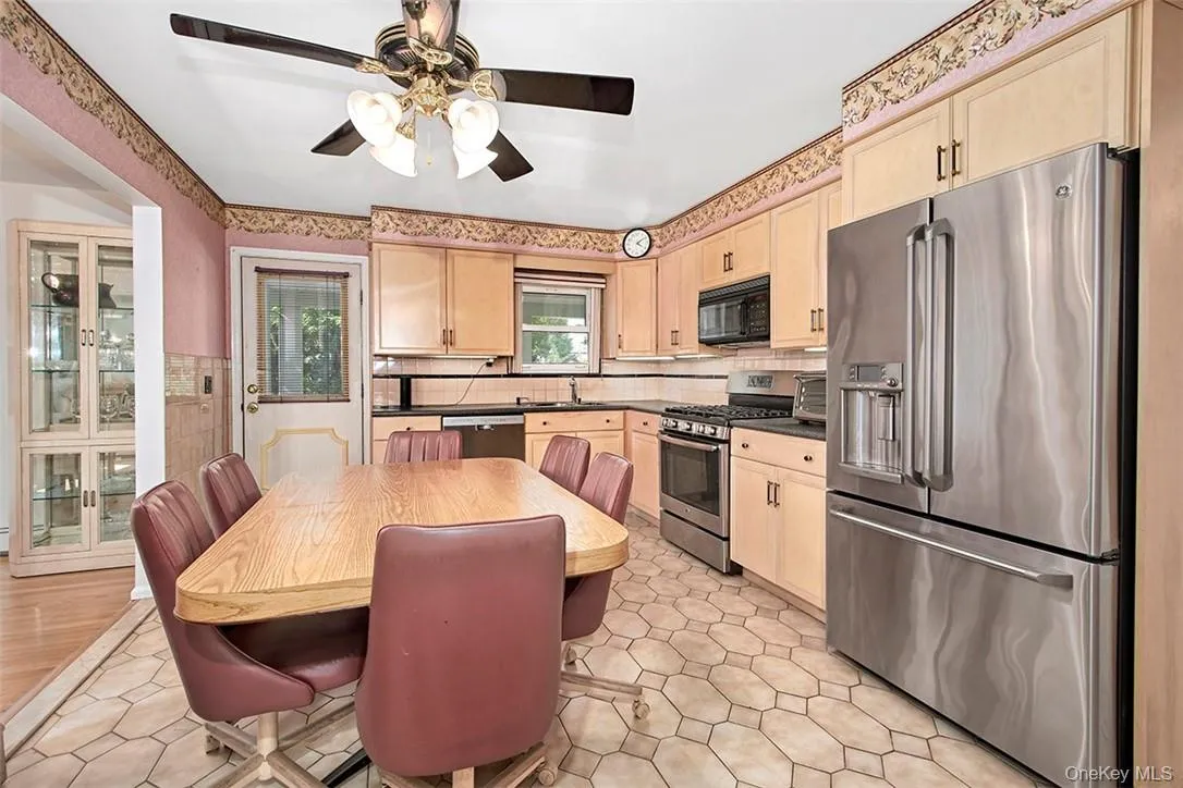 Kitchen featuring appliances with stainless steel finishes, light brown cabinets, decorative backsplash, light wood-type flooring, and ceiling fan Kitchen featuring appliances with stainless steel finishes, light brown cabinets, decorative backsplash, light wood-type flooring, and ceiling fan