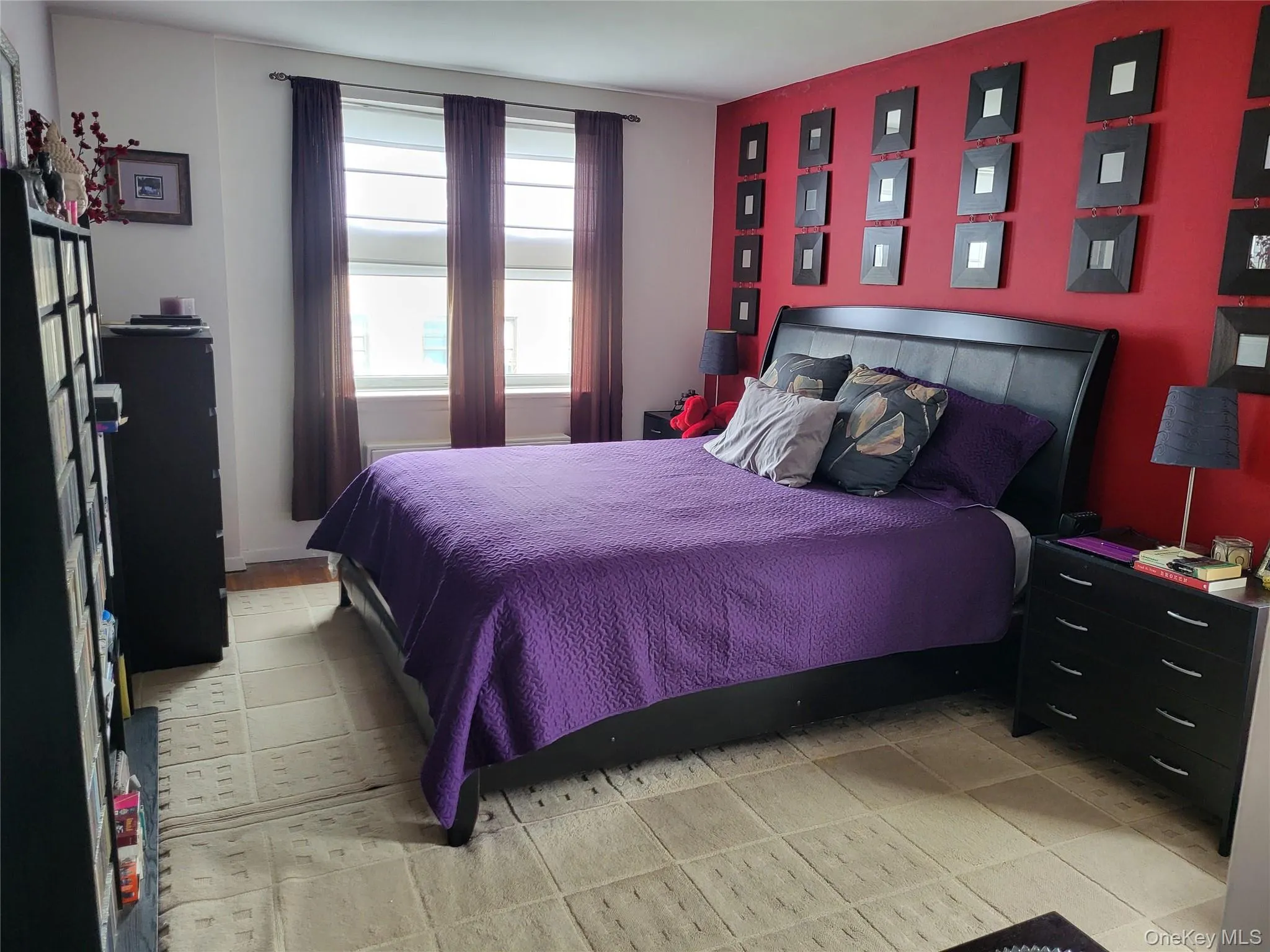 Bedroom featuring a deep red accent wall, a wide window with blinds, and a patterned area rug Bedroom featuring a deep red accent wall, a wide window with blinds, and a patterned area rug