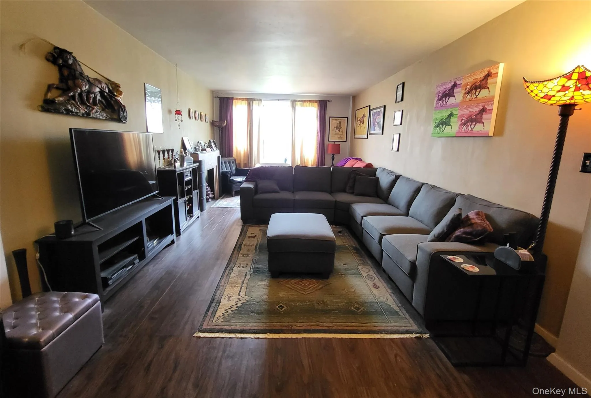 Spacious living area featuring wood-finish flooring, and ample natural light from the far window Spacious living area featuring wood-finish flooring, and ample natural light from the far window