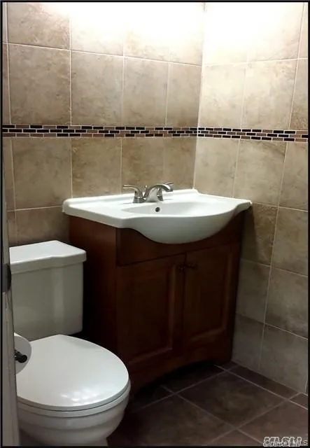 Half bathroom featuring vanity, tile walls, and dark tile patterned flooring Half bathroom featuring vanity, tile walls, and dark tile patterned flooring