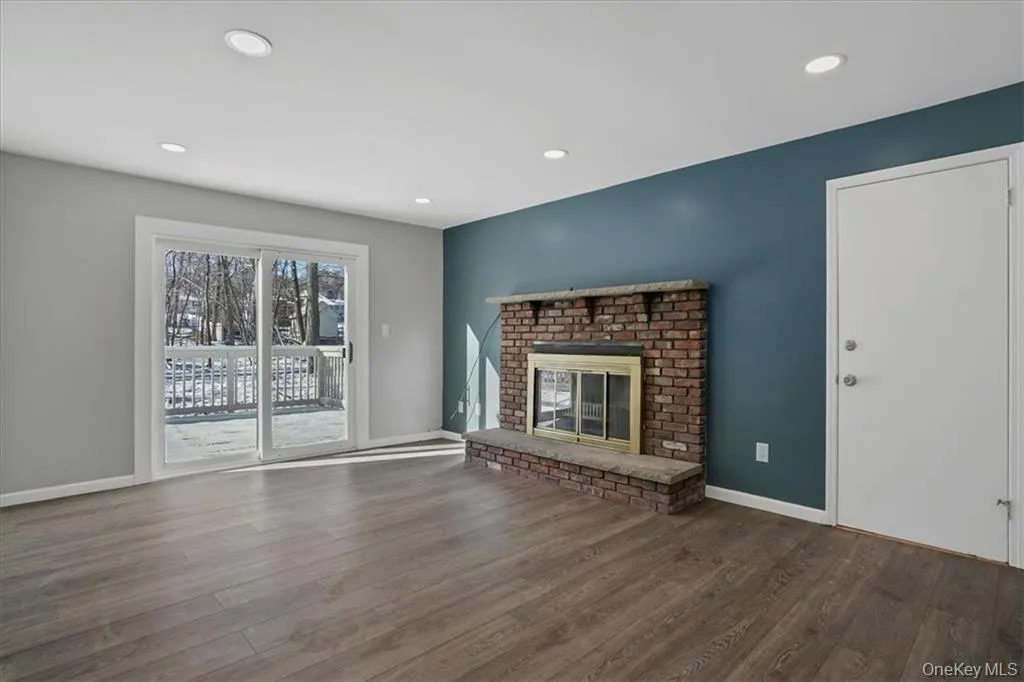 Unfurnished living room with a brick fireplace, wood finished floors, and recessed lighting Unfurnished living room with a brick fireplace, wood finished floors, and recessed lighting
