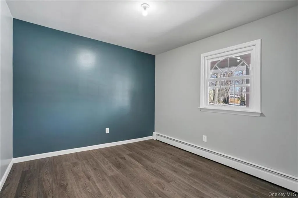Unfurnished room featuring a baseboard heating unit and dark wood finished floors Unfurnished room featuring a baseboard heating unit and dark wood finished floors