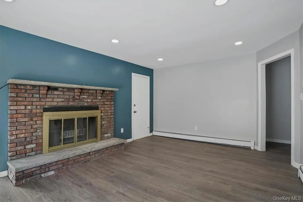 Unfurnished living room with baseboard heating, wood finished floors, recessed lighting, and a fireplace Unfurnished living room with baseboard heating, wood finished floors, recessed lighting, and a fireplace