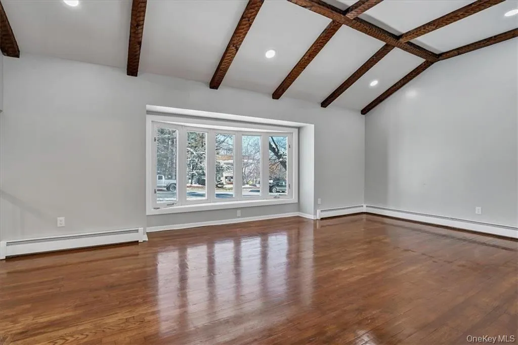 Unfurnished living room featuring dark wood-type flooring, recessed lighting, and a baseboard radiator Unfurnished living room featuring dark wood-type flooring, recessed lighting, and a baseboard radiator