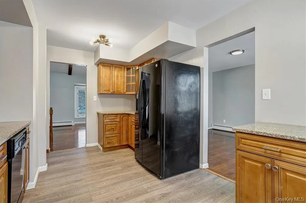 Kitchen featuring black appliances, brown cabinetry, light wood-type flooring, and light stone countertops Kitchen featuring black appliances, brown cabinetry, light wood-type flooring, and light stone countertops