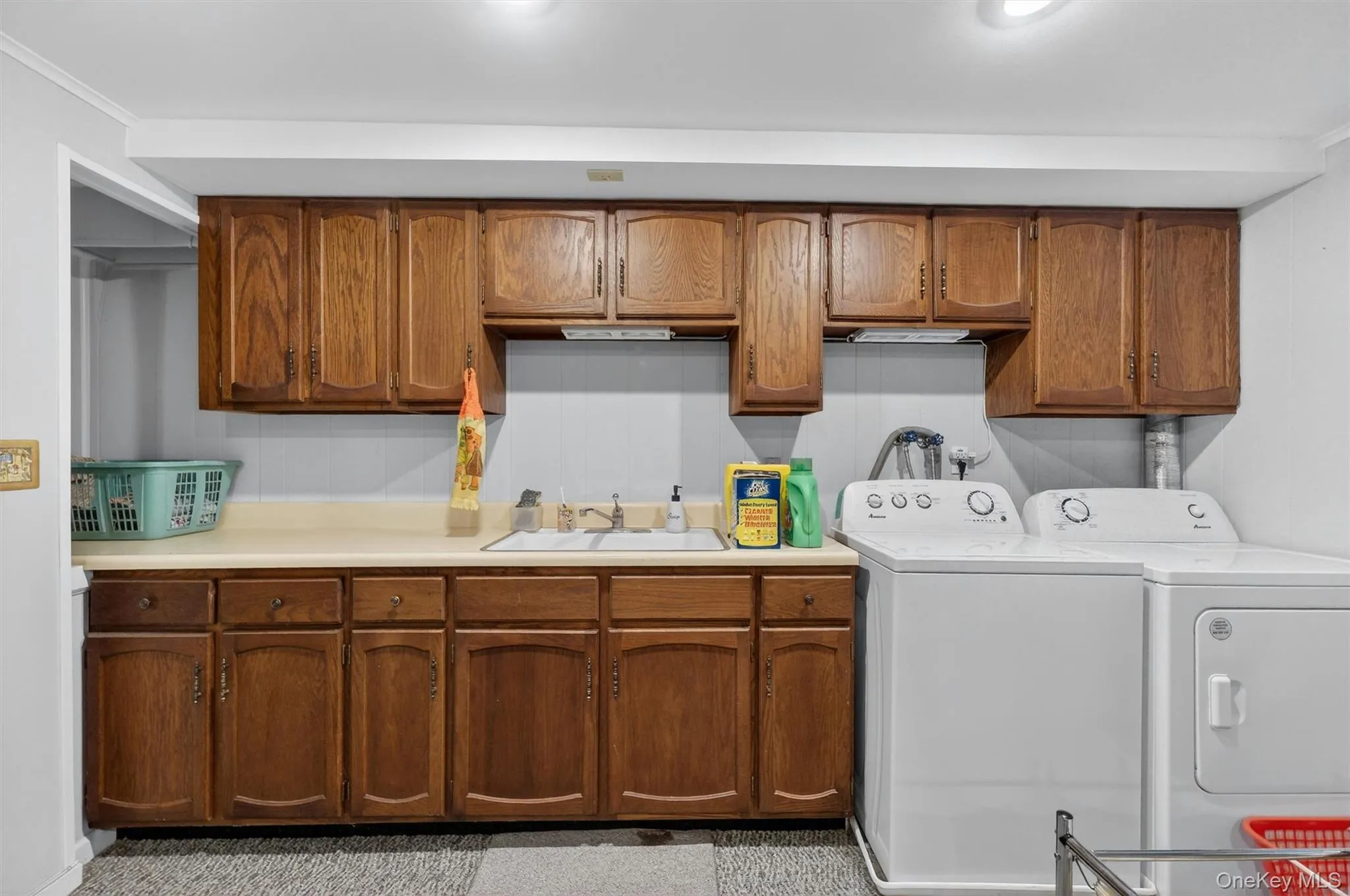 Laundry room is on the lower level, with newer appliances. It features extensive wood cabinetry, a built-in utility sink, a light-toned countertop, beadboard wall paneling, and recessed lighting Laundry room is on the lower level, with newer appliances. It features extensive wood cabinetry, a built-in utility sink, a light-toned countertop, beadboard wall paneling, and recessed lighting