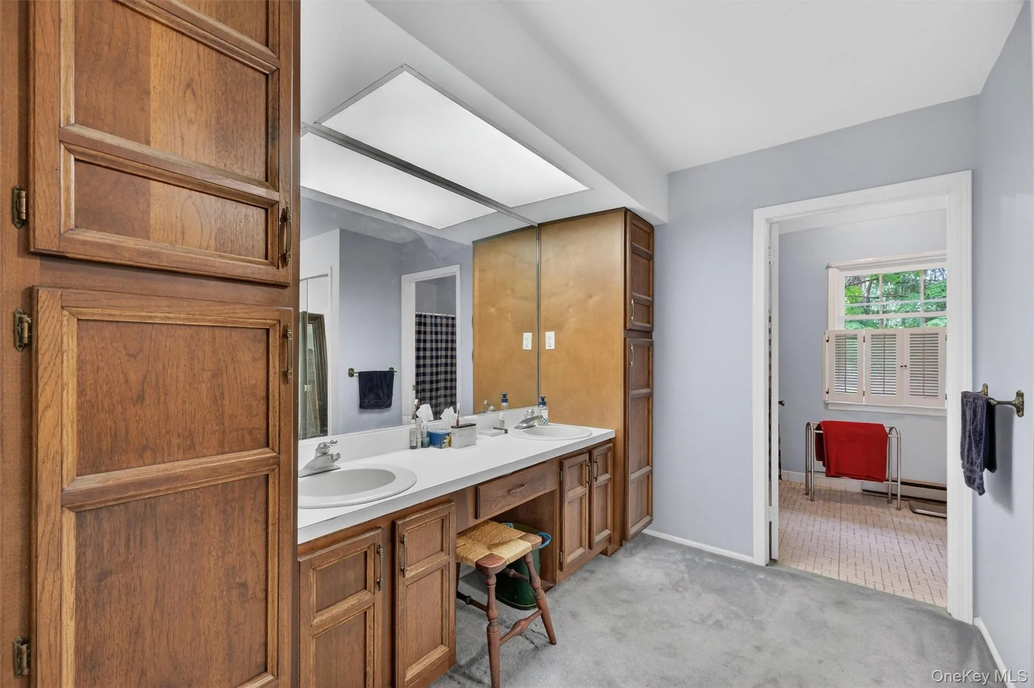 Primary Bathroom: Dual-sink vanity with wood-finish cabinetry, white countertops, and full-wall mirror Primary Bathroom: Dual-sink vanity with wood-finish cabinetry, white countertops, and full-wall mirror