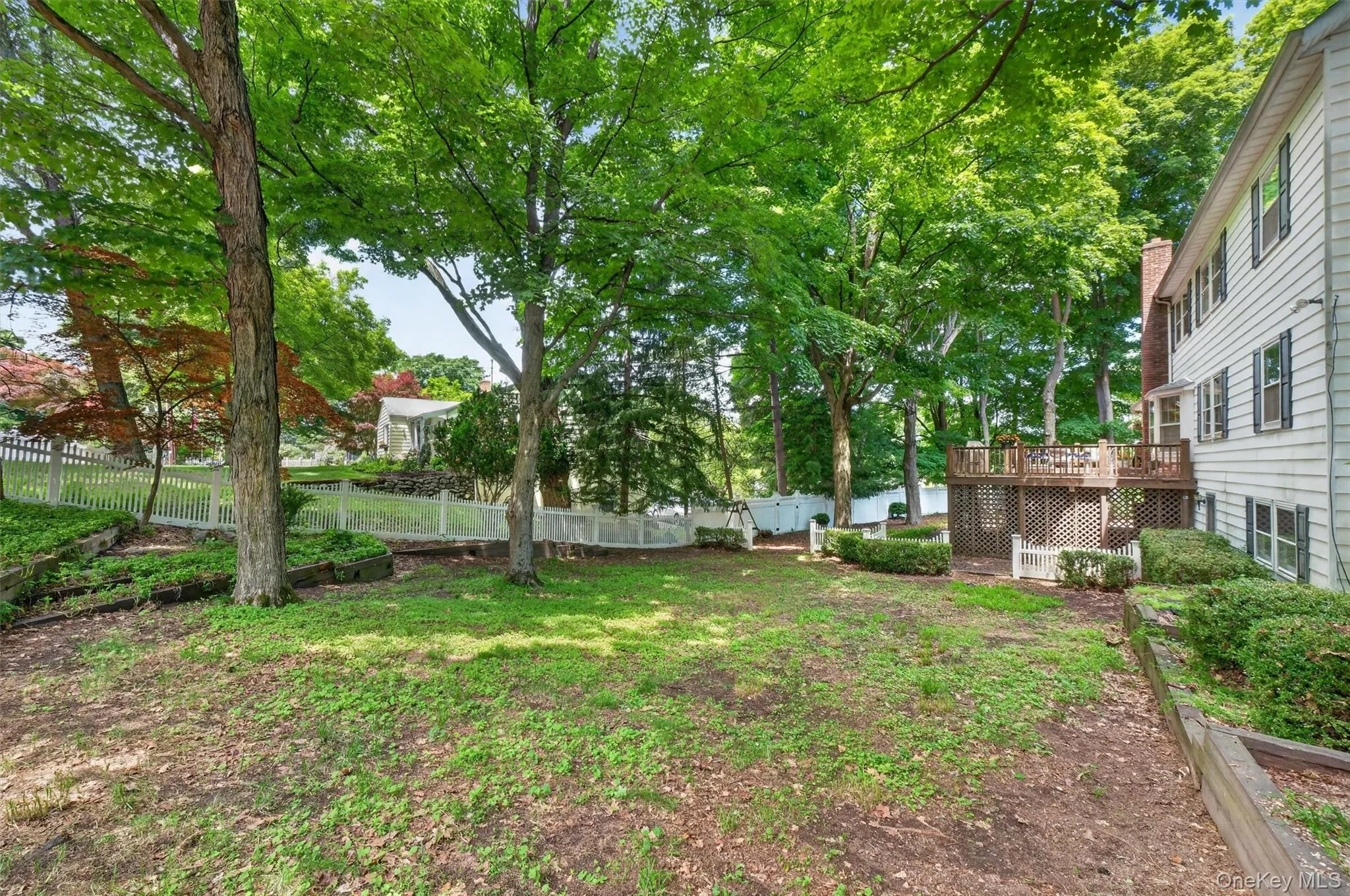 Expansive backyard featuring mature trees, a multi-level wood deck, white picket fencing, and a white siding exterior Expansive backyard featuring mature trees, a multi-level wood deck, white picket fencing, and a white siding exterior