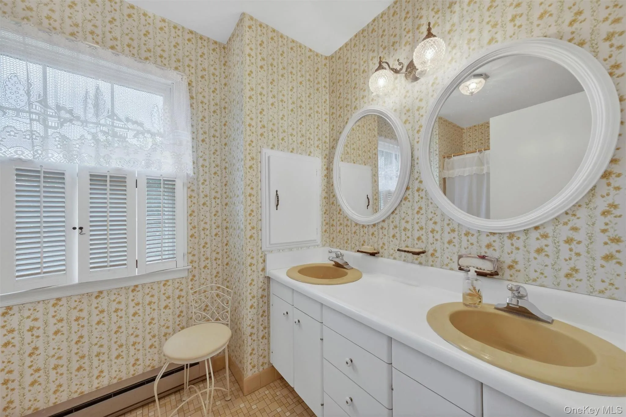 3nd floor hall bathroom: Bathroom with a double vanity featuring two inset sinks, individual oval mirrors with white frames, and a wall-mounted light fixture with two glass shades 3nd floor hall bathroom: Bathroom with a double vanity featuring two inset sinks, individual oval mirrors with white frames, and a wall-mounted light fixture with two glass shades