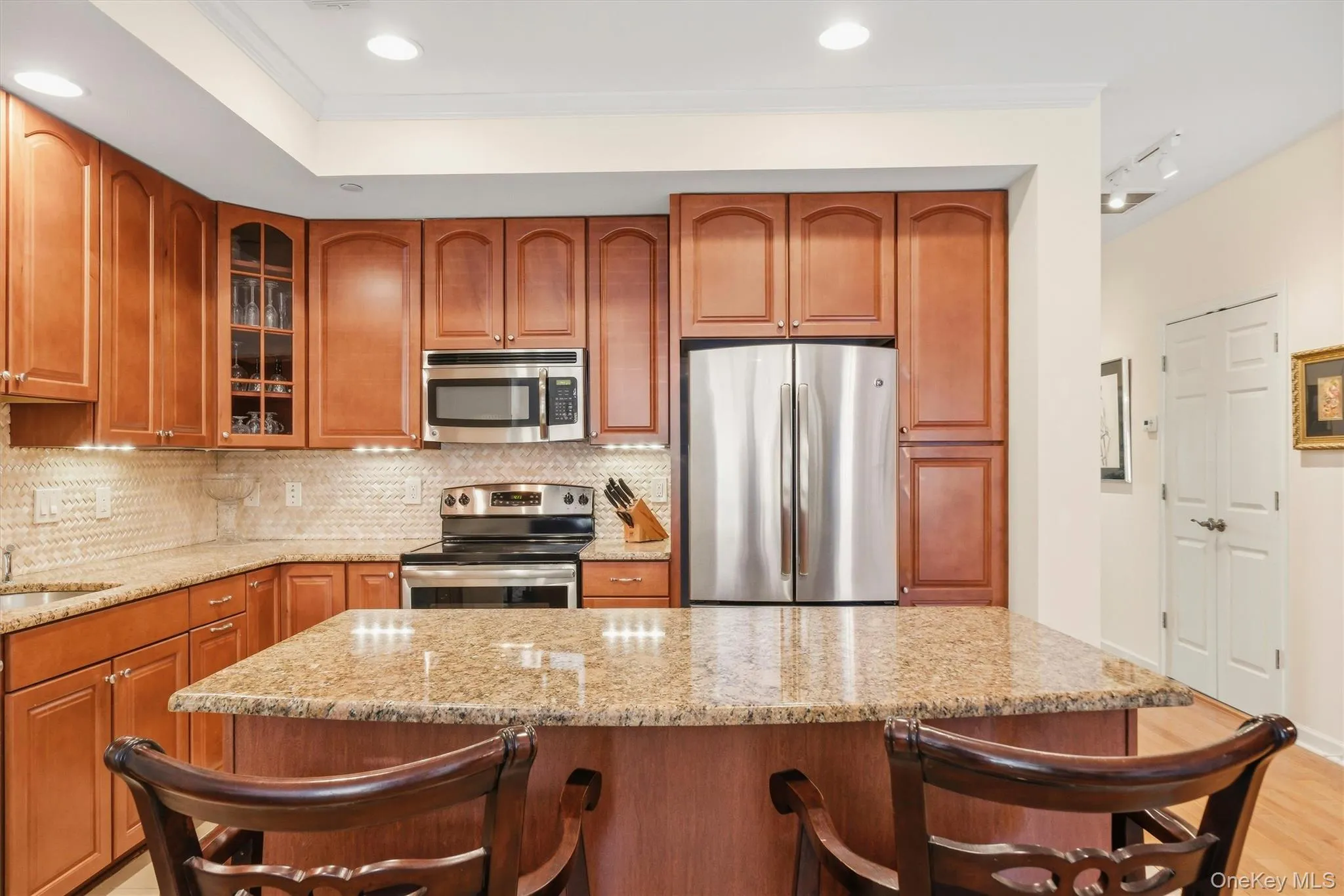 Beautifully updated kitchen showcasing granite countertops, stainless steel appliances, recessed lighting, a center island, abundant wood cabinetry, and a cream arched herringbone marble mosaic backsplash. Beautifully updated kitchen showcasing granite countertops, stainless steel appliances, recessed lighting, a center island, abundant wood cabinetry, and a cream arched herringbone marble mosaic backsplash.