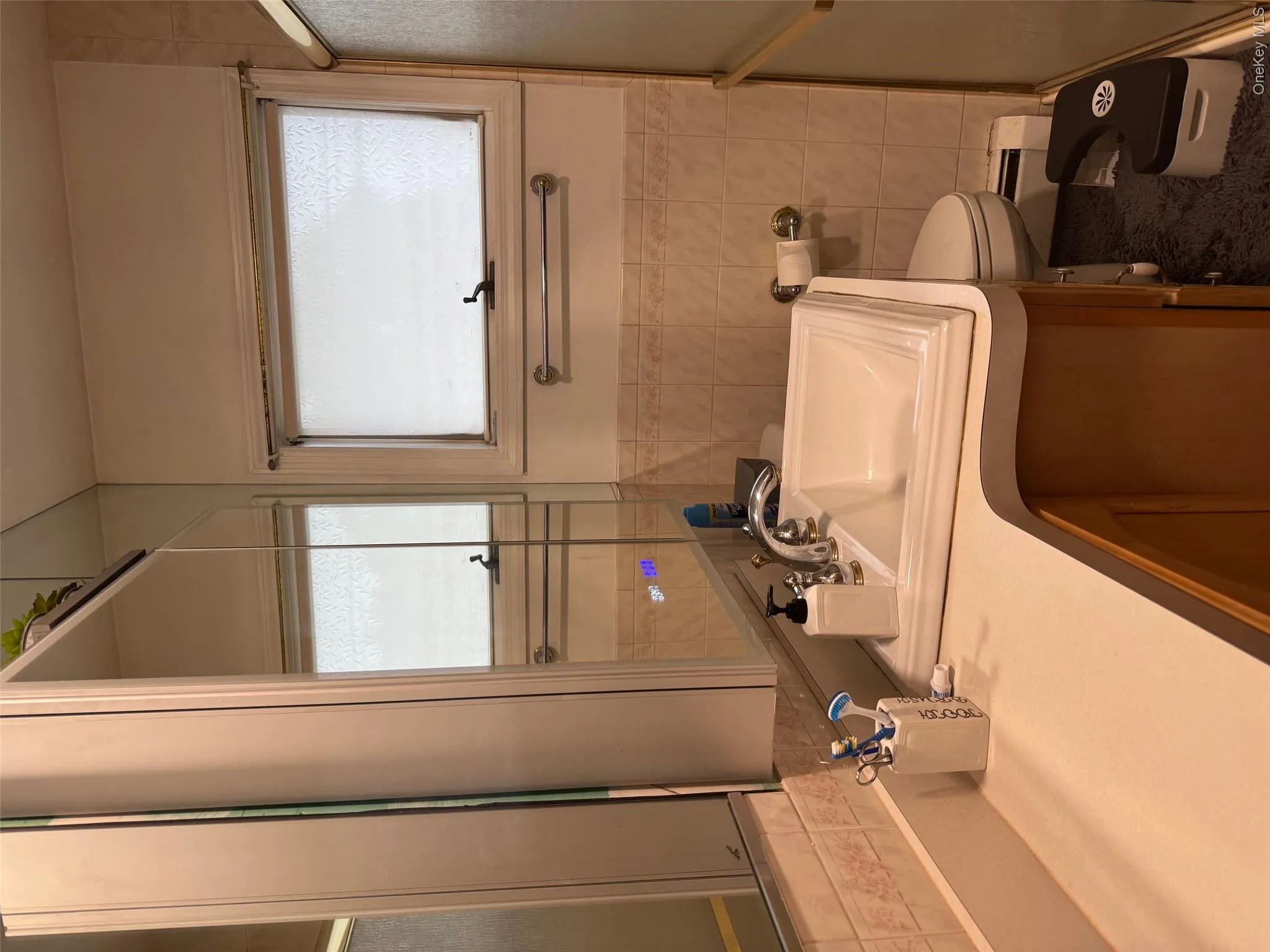 Full bath featuring healthy amount of natural light, vanity, tile walls, a baseboard heating unit, and an enclosed shower Full bath featuring healthy amount of natural light, vanity, tile walls, a baseboard heating unit, and an enclosed shower
