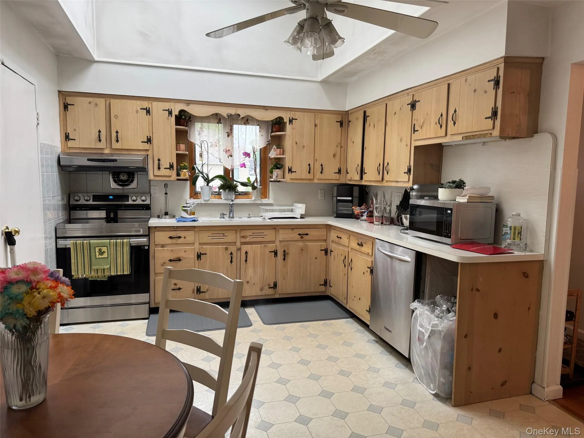 Kitchen featuring stainless steel appliances, open shelves, ceiling fan, light countertops, and a sink Kitchen featuring stainless steel appliances, open shelves, ceiling fan, light countertops, and a sink