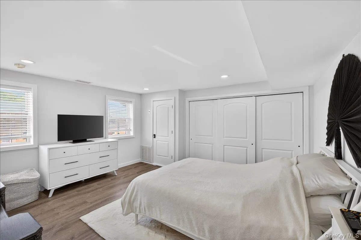 Bedroom featuring wood-finish flooring, two large windows with blinds, recessed lighting, and a spacious built-in sliding closet Bedroom featuring wood-finish flooring, two large windows with blinds, recessed lighting, and a spacious built-in sliding closet