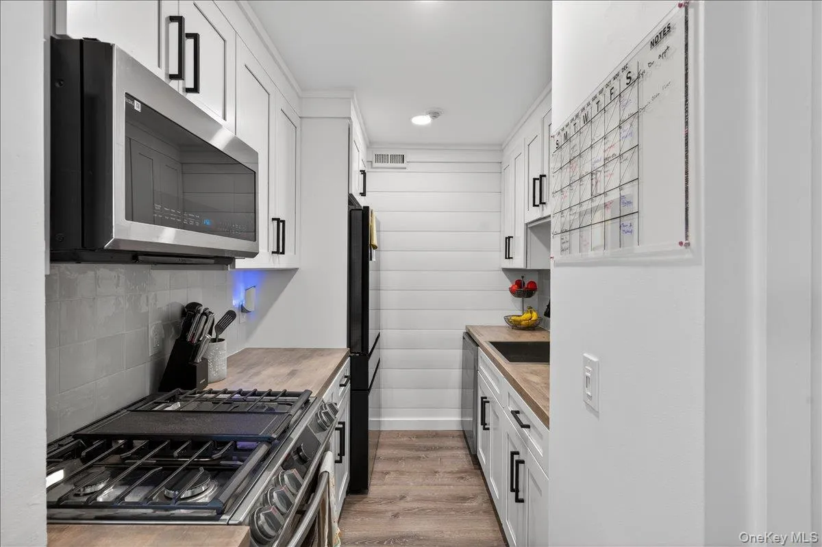 Galley kitchen featuring white cabinetry with black hardware, wood-finish countertops, stainless steel appliances, and wood-finish flooring Galley kitchen featuring white cabinetry with black hardware, wood-finish countertops, stainless steel appliances, and wood-finish flooring