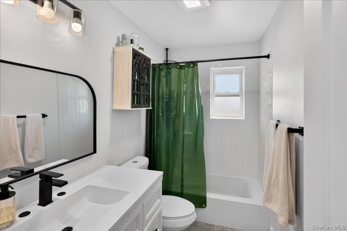 Bathroom featuring a white vanity with integrated sink, black fixtures, and a contemporary arched mirror Bathroom featuring a white vanity with integrated sink, black fixtures, and a contemporary arched mirror