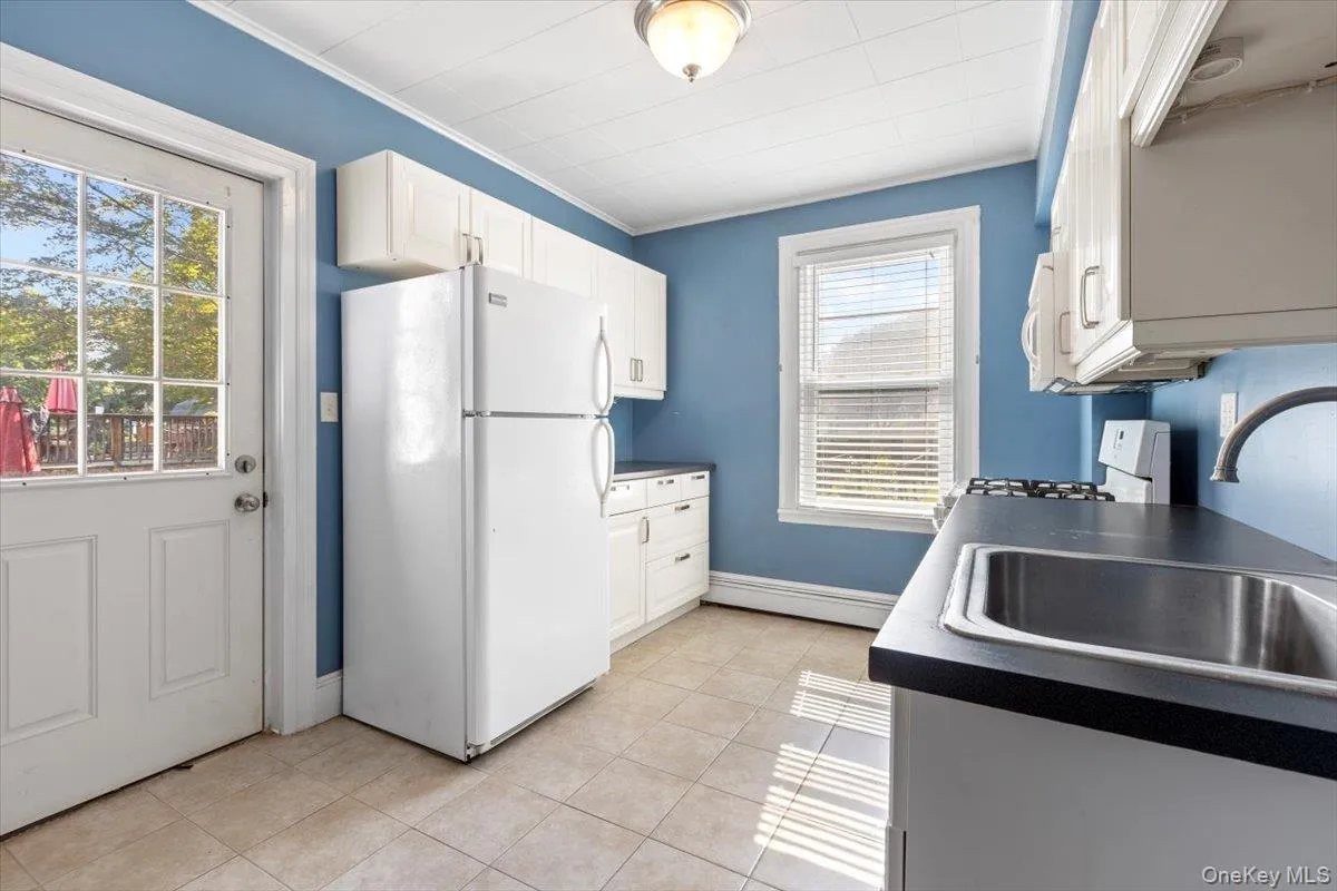 Kitchen featuring light tile patterned floors, white cabinetry, a sink, a baseboard radiator, and white appliances Kitchen featuring light tile patterned floors, white cabinetry, a sink, a baseboard radiator, and white appliances