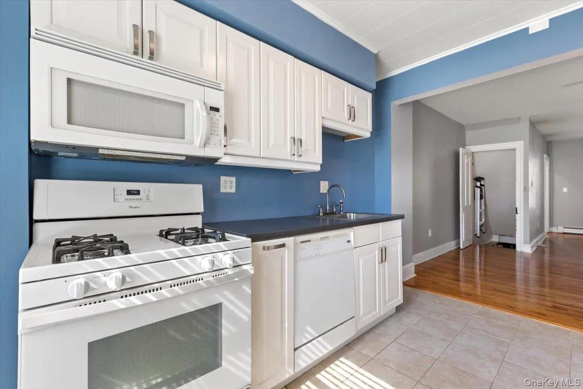 Kitchen with white cabinetry, dark countertops, white appliances, and a sink Kitchen with white cabinetry, dark countertops, white appliances, and a sink