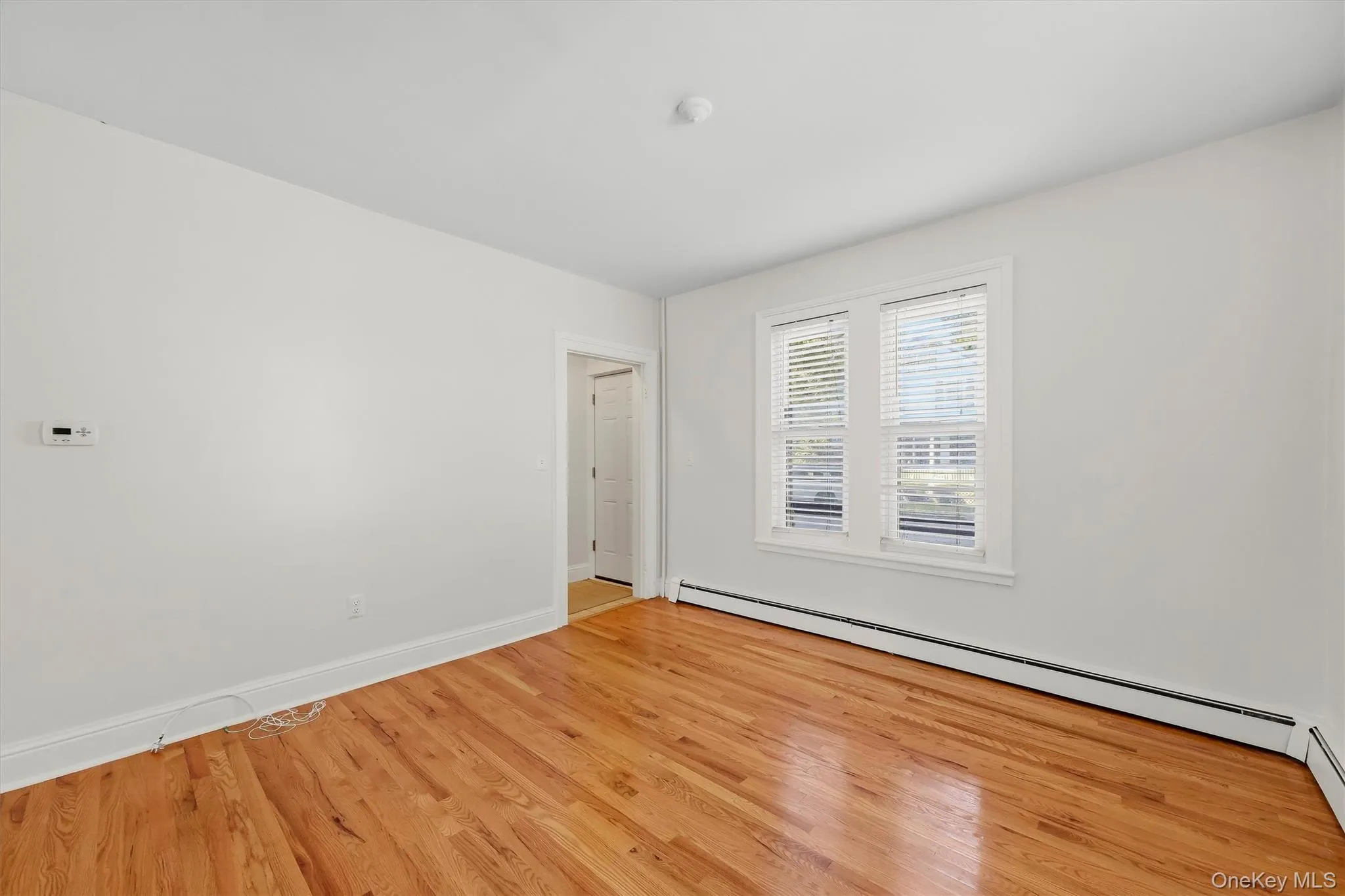 Wood-finish flooring with white baseboard trim, white walls, and a pair of double-hung windows Wood-finish flooring with white baseboard trim, white walls, and a pair of double-hung windows