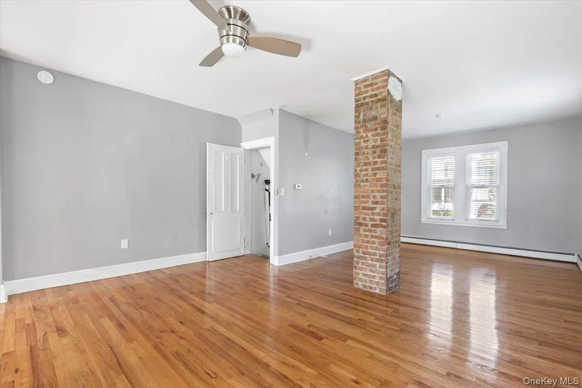 Unfurnished living room featuring baseboard heating, decorative columns, and light wood-style flooring Unfurnished living room featuring baseboard heating, decorative columns, and light wood-style flooring