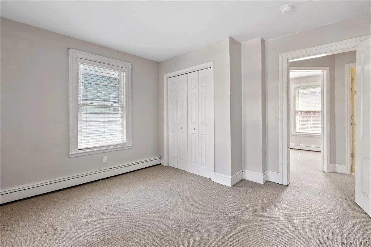 Unfurnished bedroom featuring a baseboard heating unit, multiple windows, and carpet Unfurnished bedroom featuring a baseboard heating unit, multiple windows, and carpet