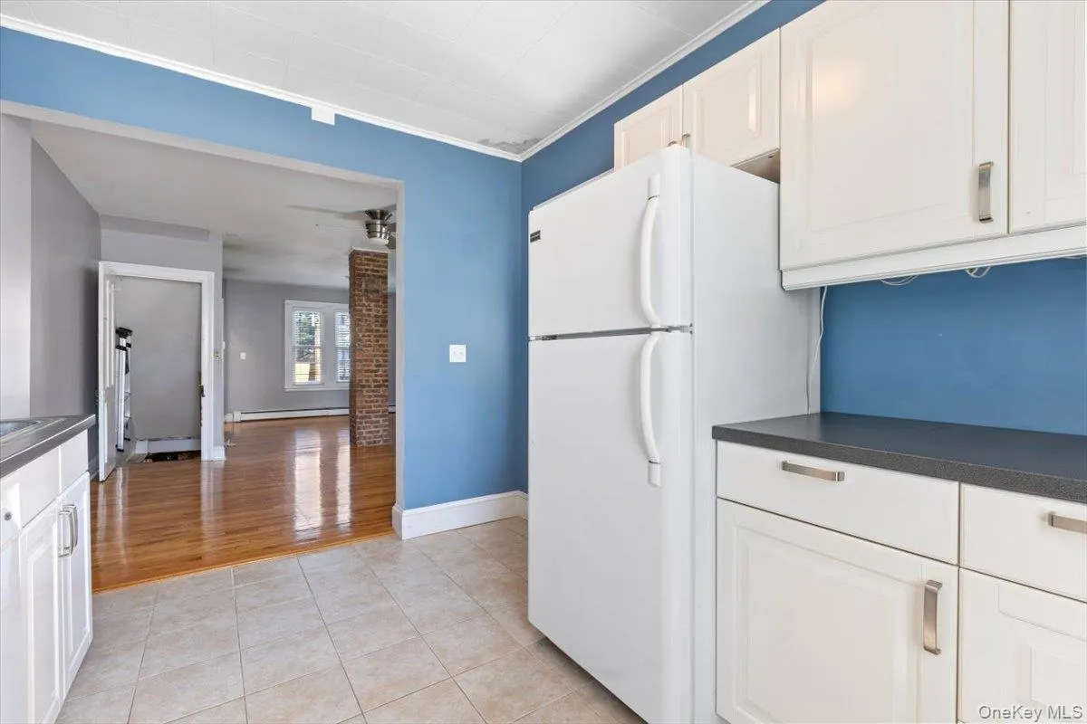 Kitchen featuring baseboard heating, dark countertops, white cabinetry, and freestanding refrigerator Kitchen featuring baseboard heating, dark countertops, white cabinetry, and freestanding refrigerator