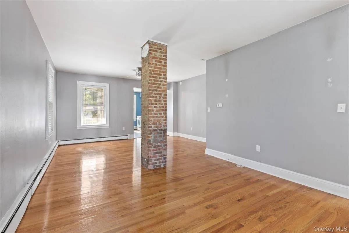 Unfurnished living room with baseboards, ornate columns, a baseboard heating unit, and light wood finished floors Unfurnished living room with baseboards, ornate columns, a baseboard heating unit, and light wood finished floors