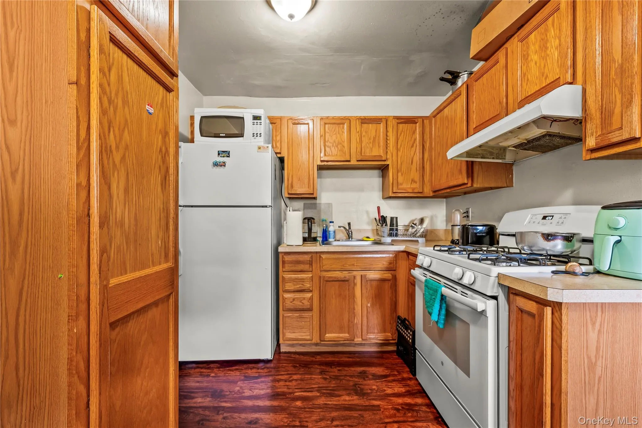 Kitchen featuring white appliances, under cabinet range hood, dark wood-type flooring, and light countertops Kitchen featuring white appliances, under cabinet range hood, dark wood-type flooring, and light countertops