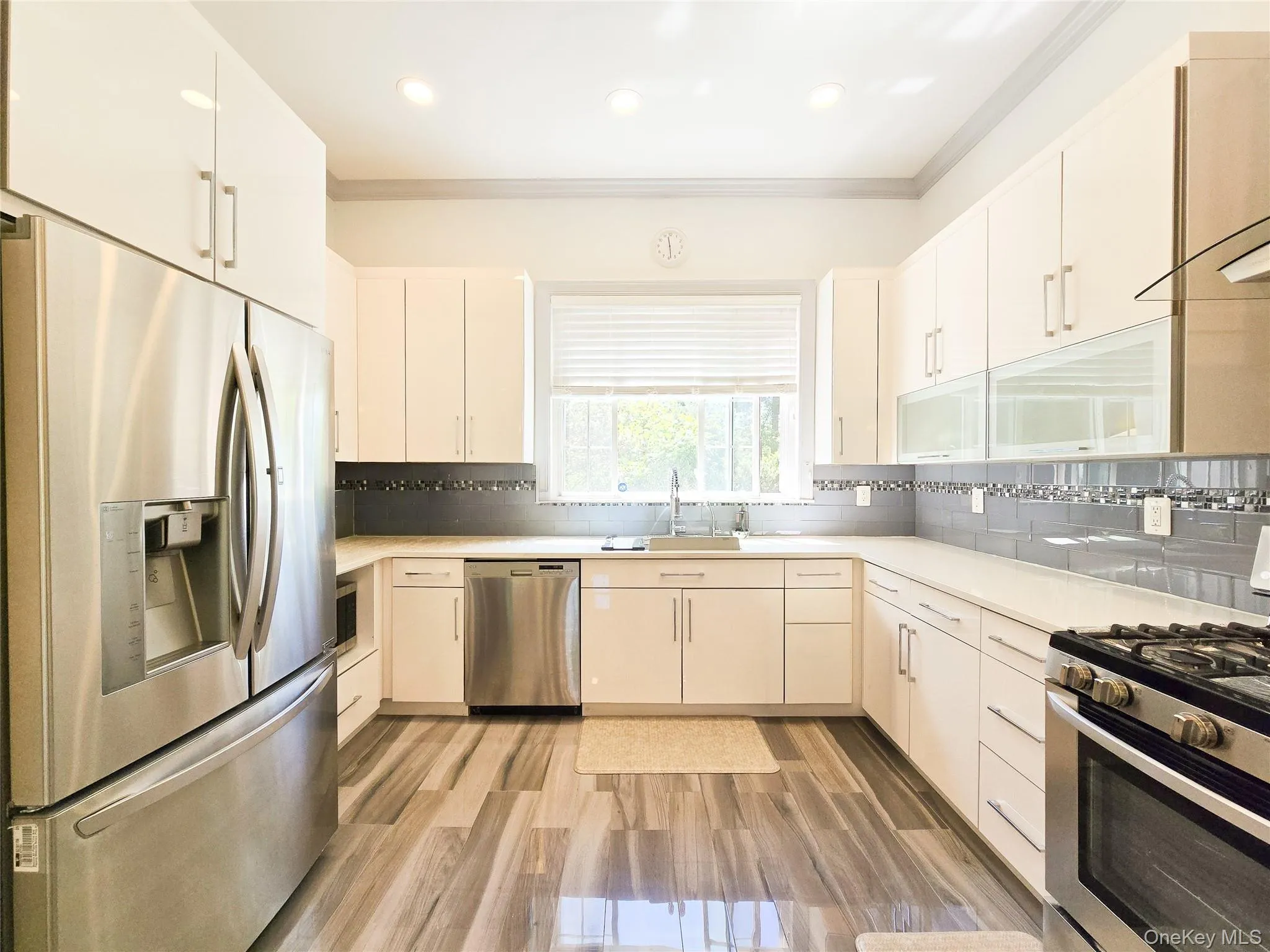 Modern kitchen featuring stainless steel appliances, white cabinetry, wood-finish flooring, and a subway tile backsplash Modern kitchen featuring stainless steel appliances, white cabinetry, wood-finish flooring, and a subway tile backsplash