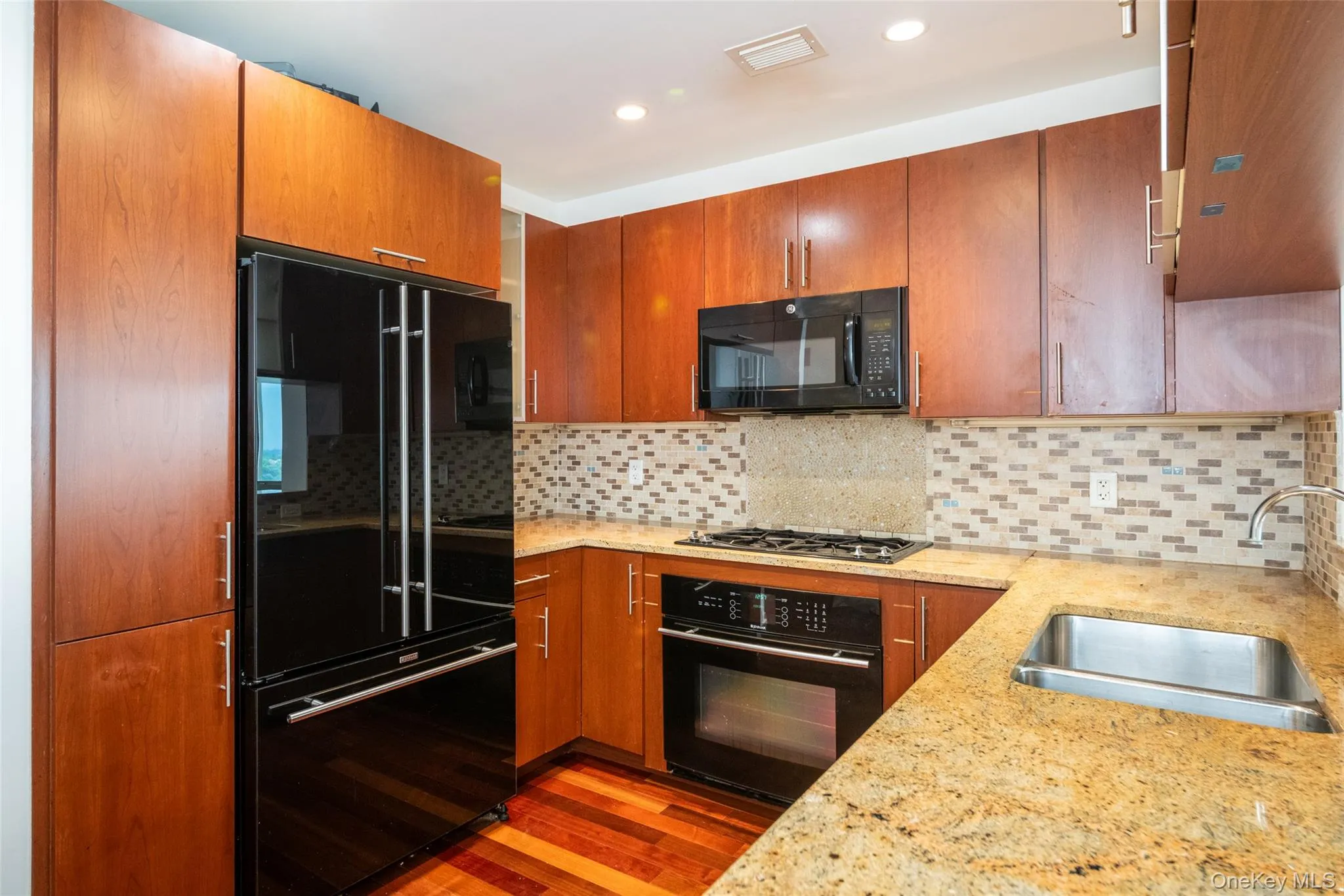 Kitchen with black appliances, wood finished floors, tasteful backsplash, light stone counters, and recessed lighting Kitchen with black appliances, wood finished floors, tasteful backsplash, light stone counters, and recessed lighting
