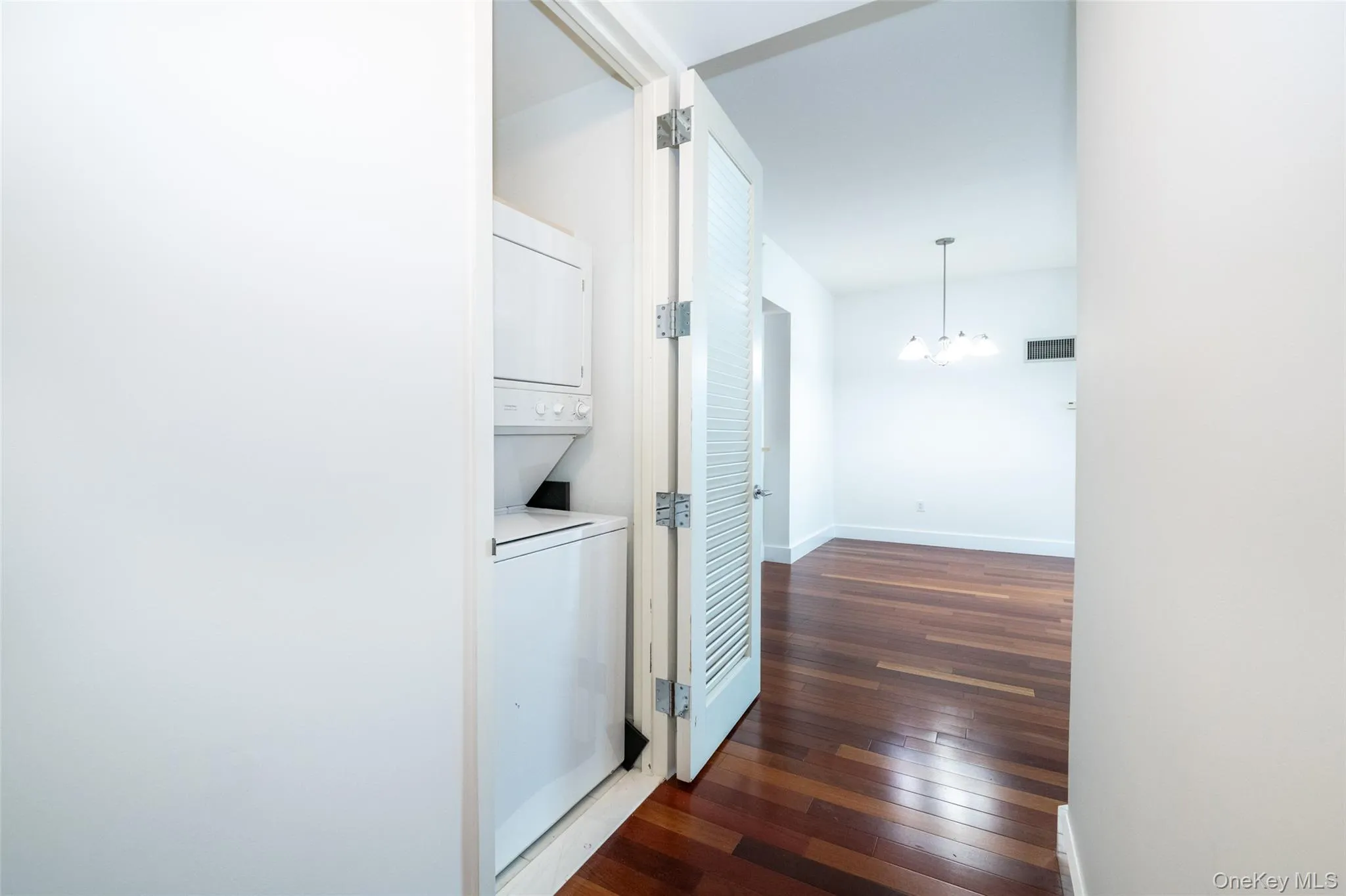 Corridor featuring stacked washer / dryer, dark wood-style floors, and a chandelier Corridor featuring stacked washer / dryer, dark wood-style floors, and a chandelier