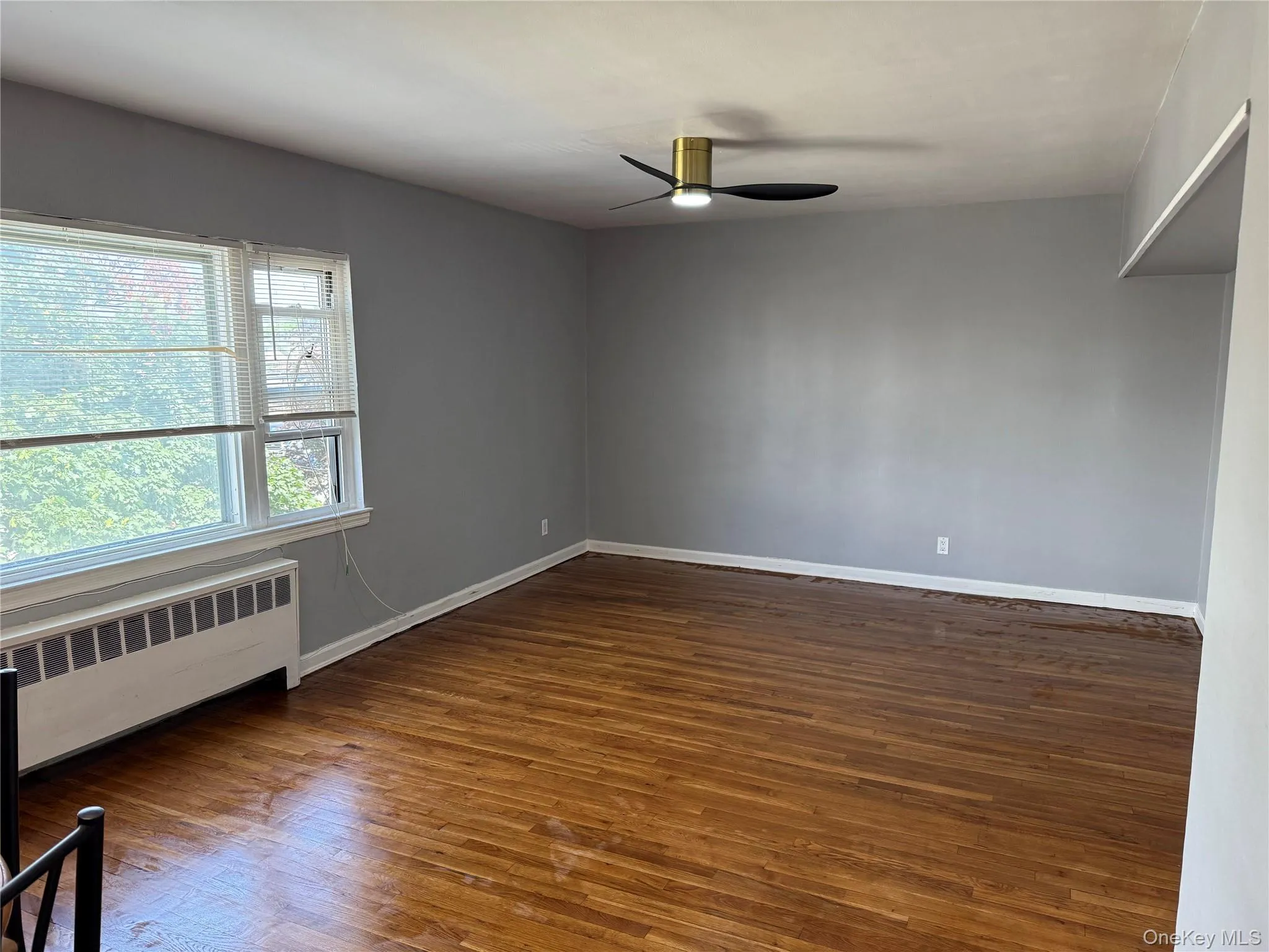 Unfurnished room with radiator heating unit, wood finished floors, and a ceiling fan Unfurnished room with radiator heating unit, wood finished floors, and a ceiling fan