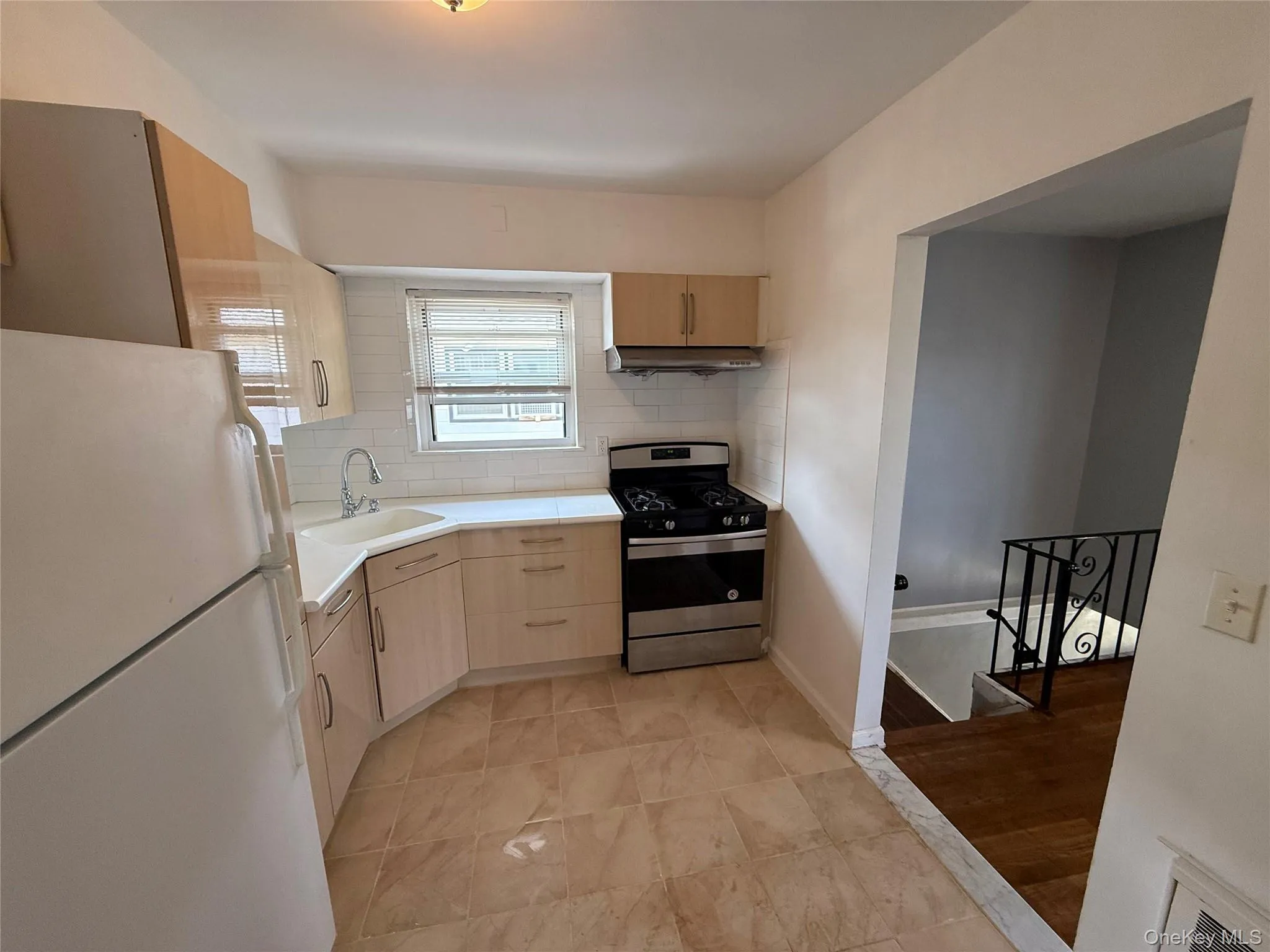 Kitchen featuring freestanding refrigerator, stainless steel gas range oven, under cabinet range hood, light countertops, and backsplash Kitchen featuring freestanding refrigerator, stainless steel gas range oven, under cabinet range hood, light countertops, and backsplash