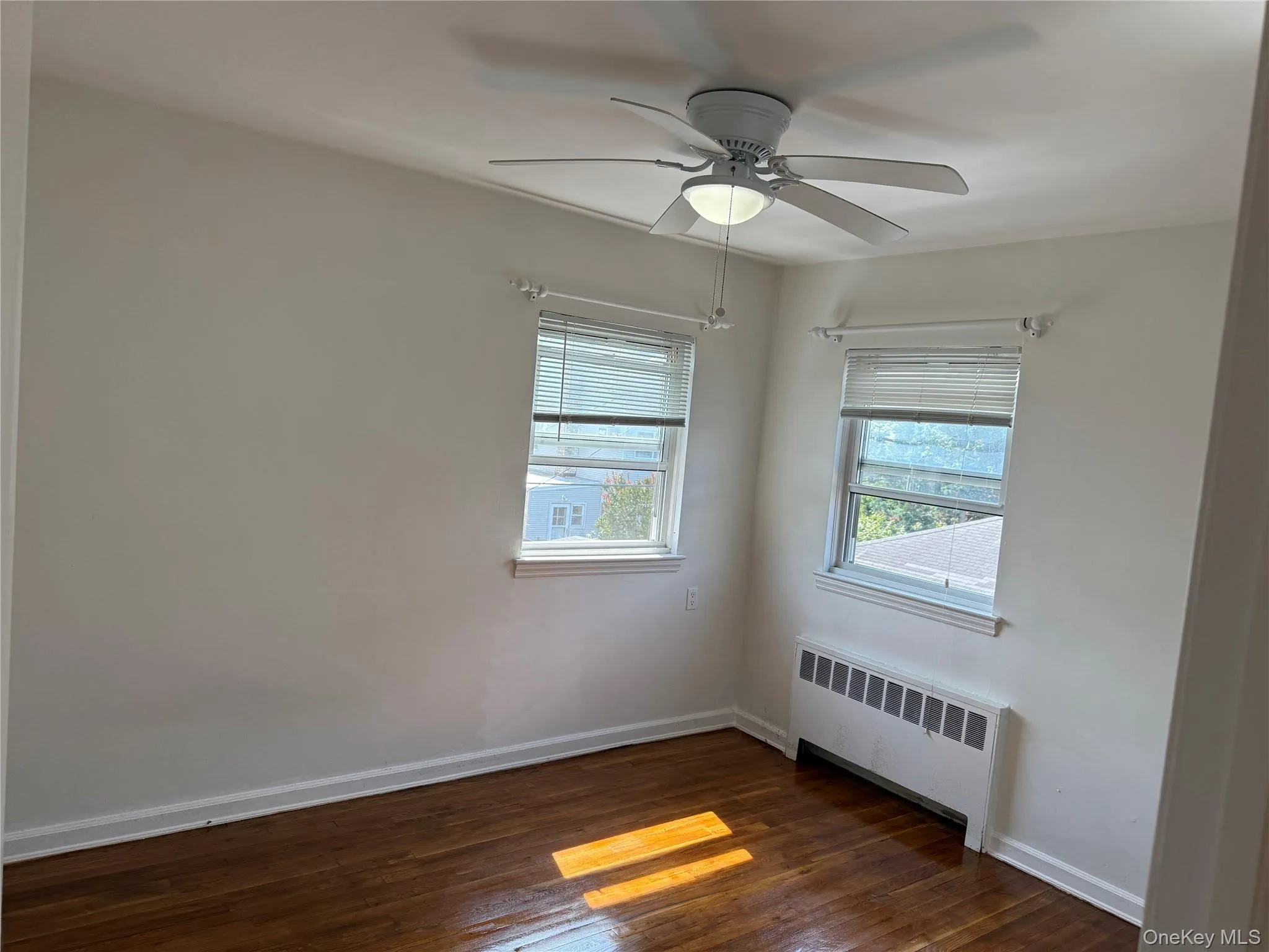 Spare room featuring radiator heating unit, dark wood-style flooring, and a ceiling fan Spare room featuring radiator heating unit, dark wood-style flooring, and a ceiling fan