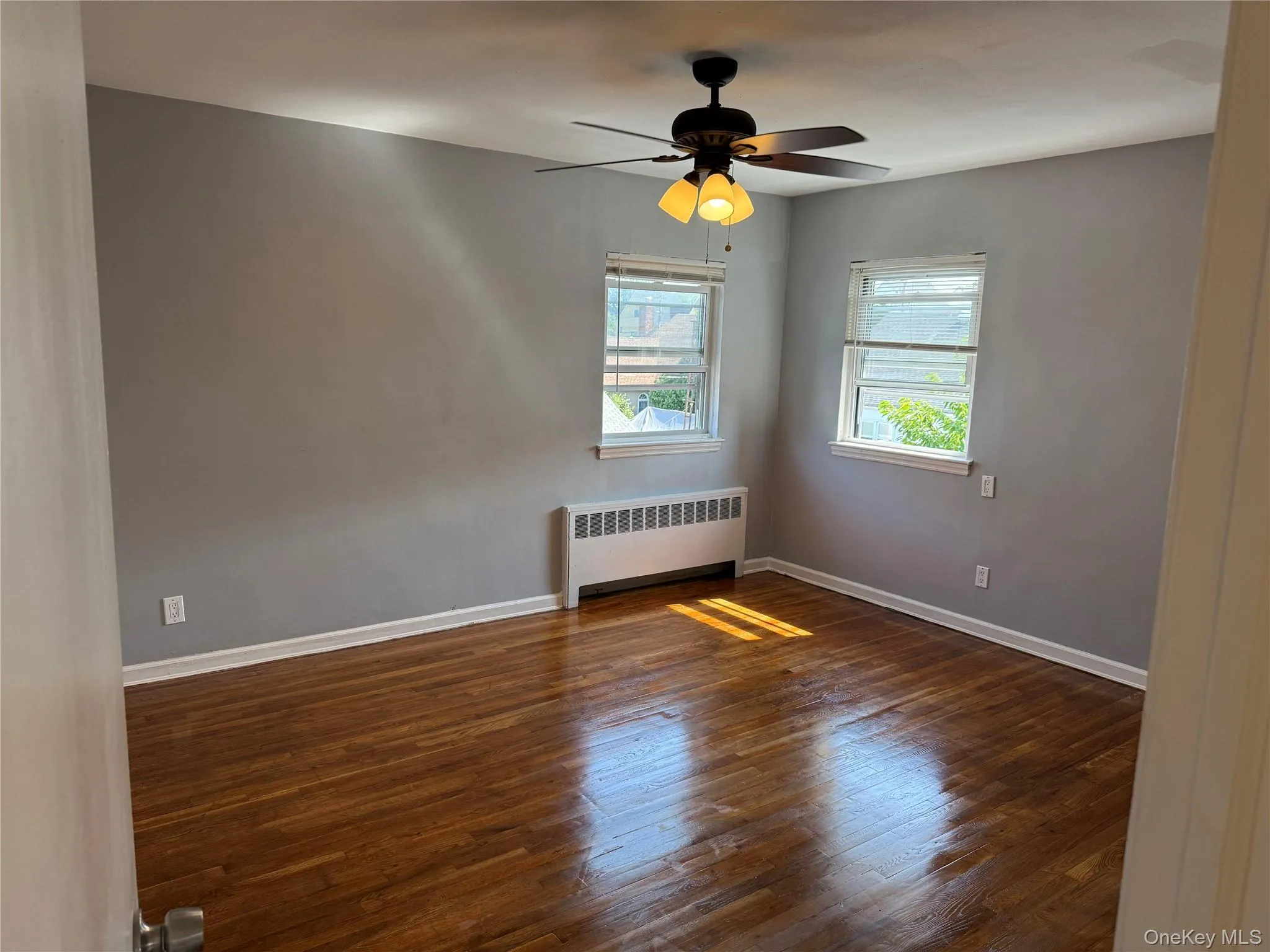Spare room with radiator, wood finished floors, and a ceiling fan Spare room with radiator, wood finished floors, and a ceiling fan