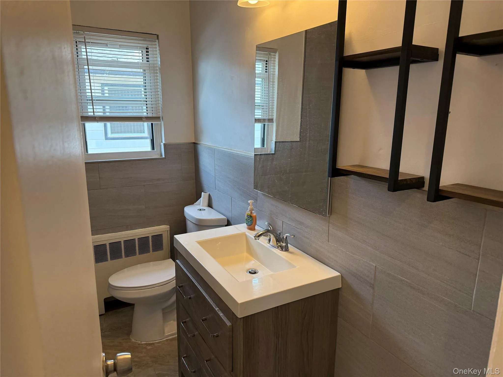 Half bath with radiator heating unit, tile walls, vanity, and plenty of natural light Half bath with radiator heating unit, tile walls, vanity, and plenty of natural light