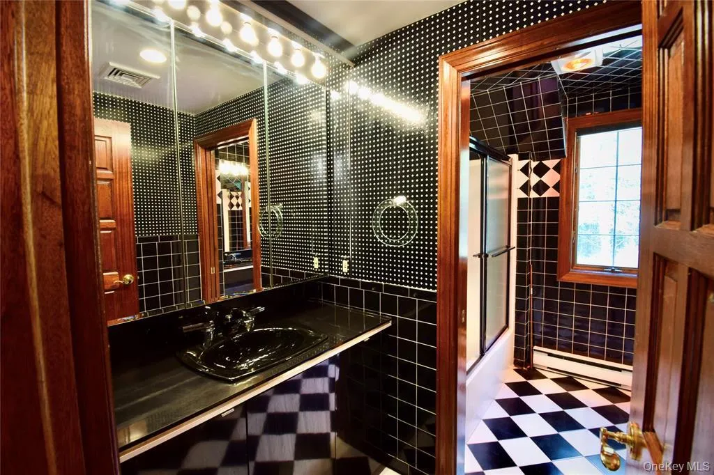 Bathroom featuring tile walls,a baseboard radiator, vanity,enclosed tub / shower combo,and tile patterned floors Bathroom featuring tile walls,a baseboard radiator, vanity,enclosed tub / shower combo,and tile patterned floors