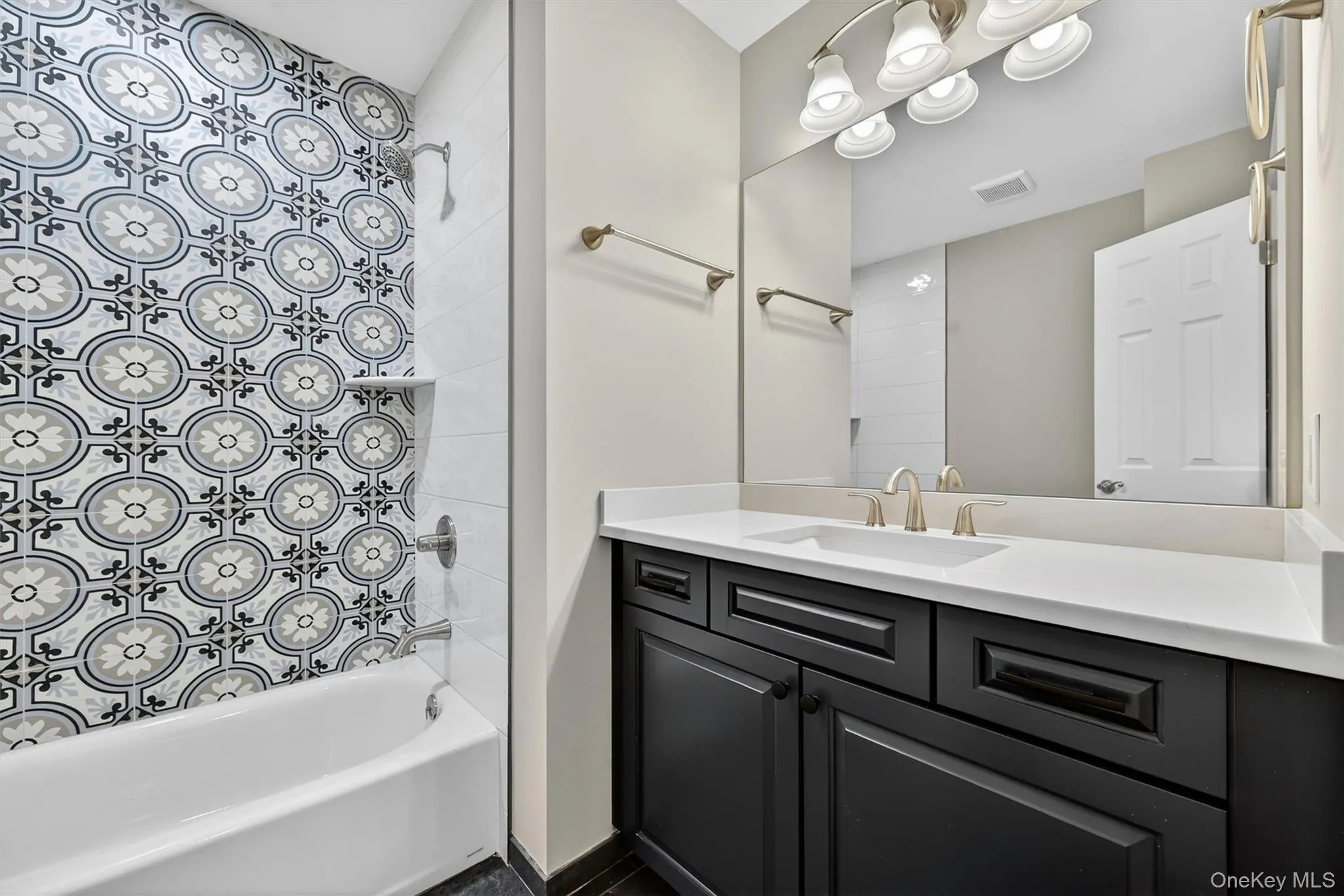 Bathroom featuring a patterned tile shower surround, a white bathtub, a dark wood-finish vanity with a white countertop, and brushed nickel fixtures Bathroom featuring a patterned tile shower surround, a white bathtub, a dark wood-finish vanity with a white countertop, and brushed nickel fixtures