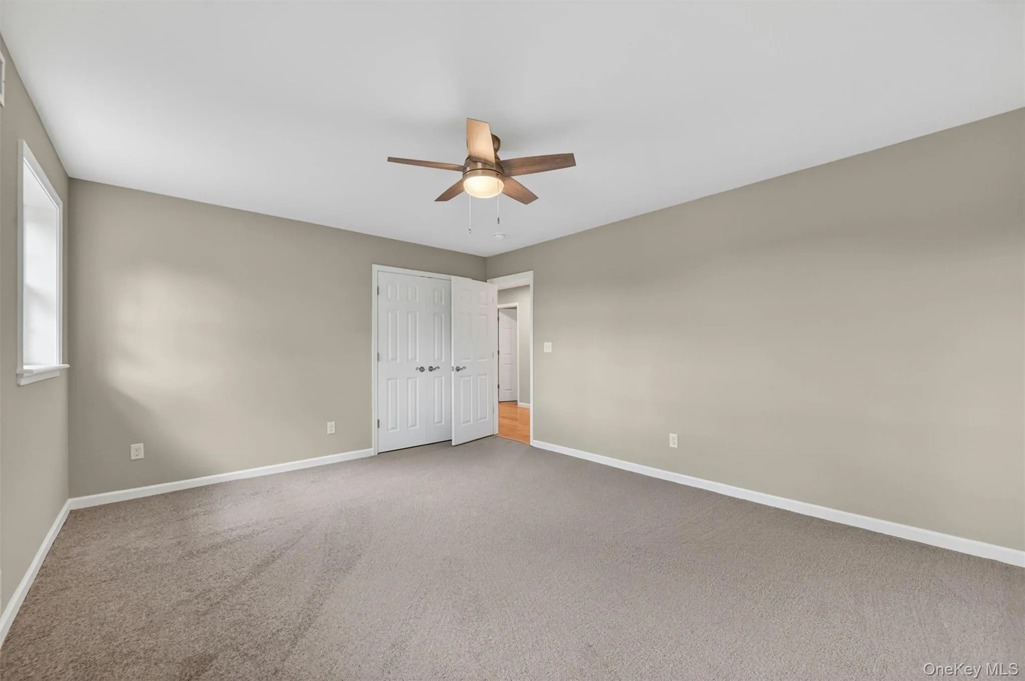 Neutral-toned room featuring a ceiling fan with light fixture, carpeted flooring, and a white-framed window Neutral-toned room featuring a ceiling fan with light fixture, carpeted flooring, and a white-framed window