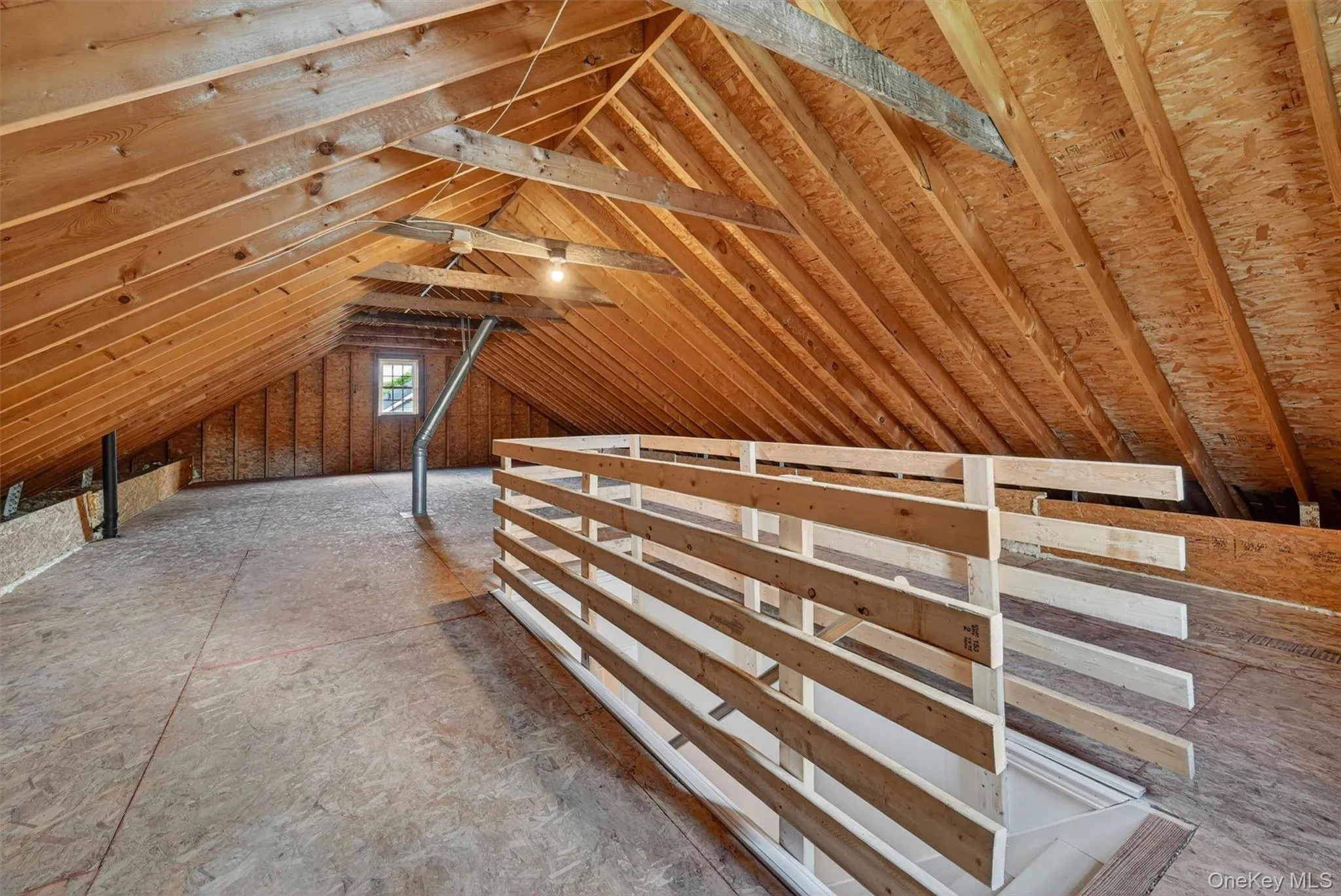 Spacious unfinished attic space featuring exposed wood rafter framing, oriented strand board flooring, and a casement window Spacious unfinished attic space featuring exposed wood rafter framing, oriented strand board flooring, and a casement window