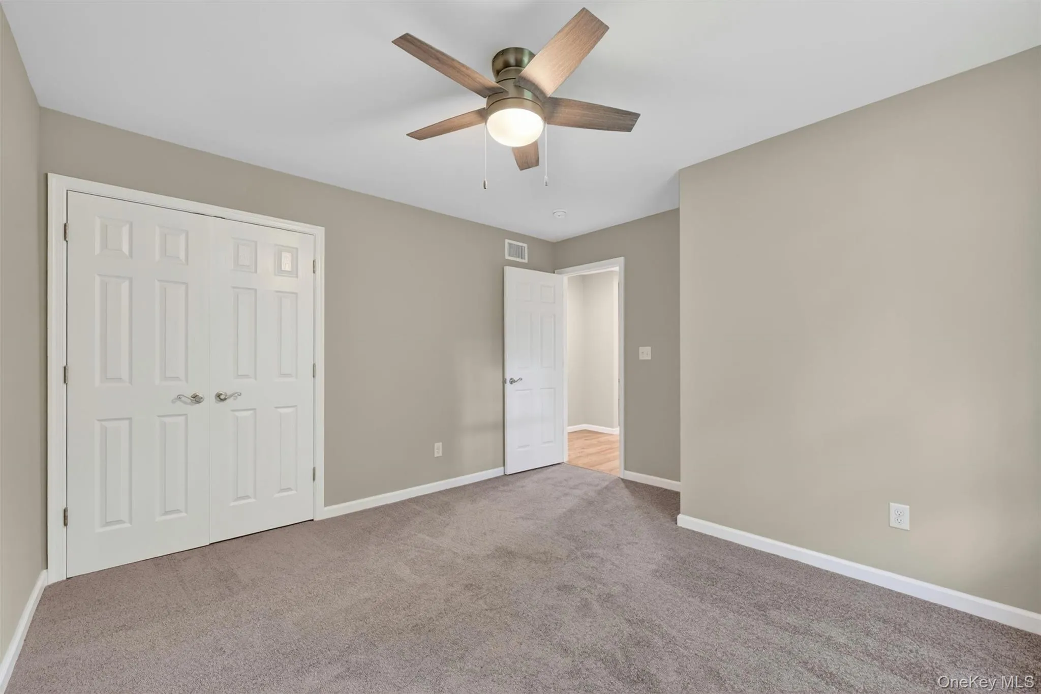 Carpeted room featuring a ceiling fan with wood-finish blades, neutral painted walls, and white trim Carpeted room featuring a ceiling fan with wood-finish blades, neutral painted walls, and white trim