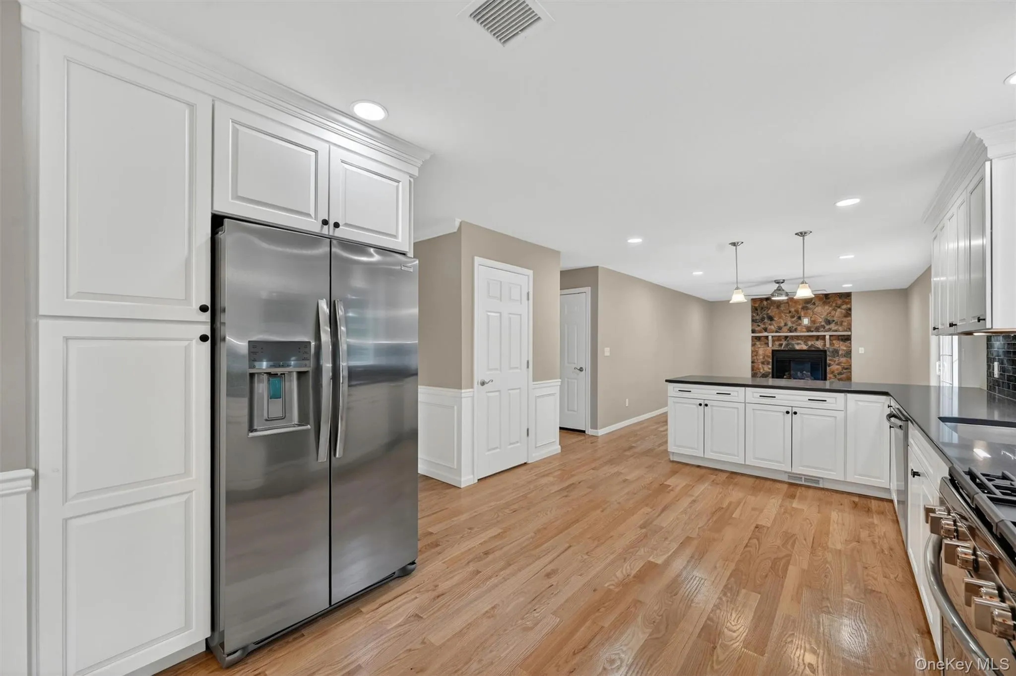 Open-concept kitchen and living area featuring wood-finish flooring, white cabinetry, dark countertops, and recessed lighting Open-concept kitchen and living area featuring wood-finish flooring, white cabinetry, dark countertops, and recessed lighting